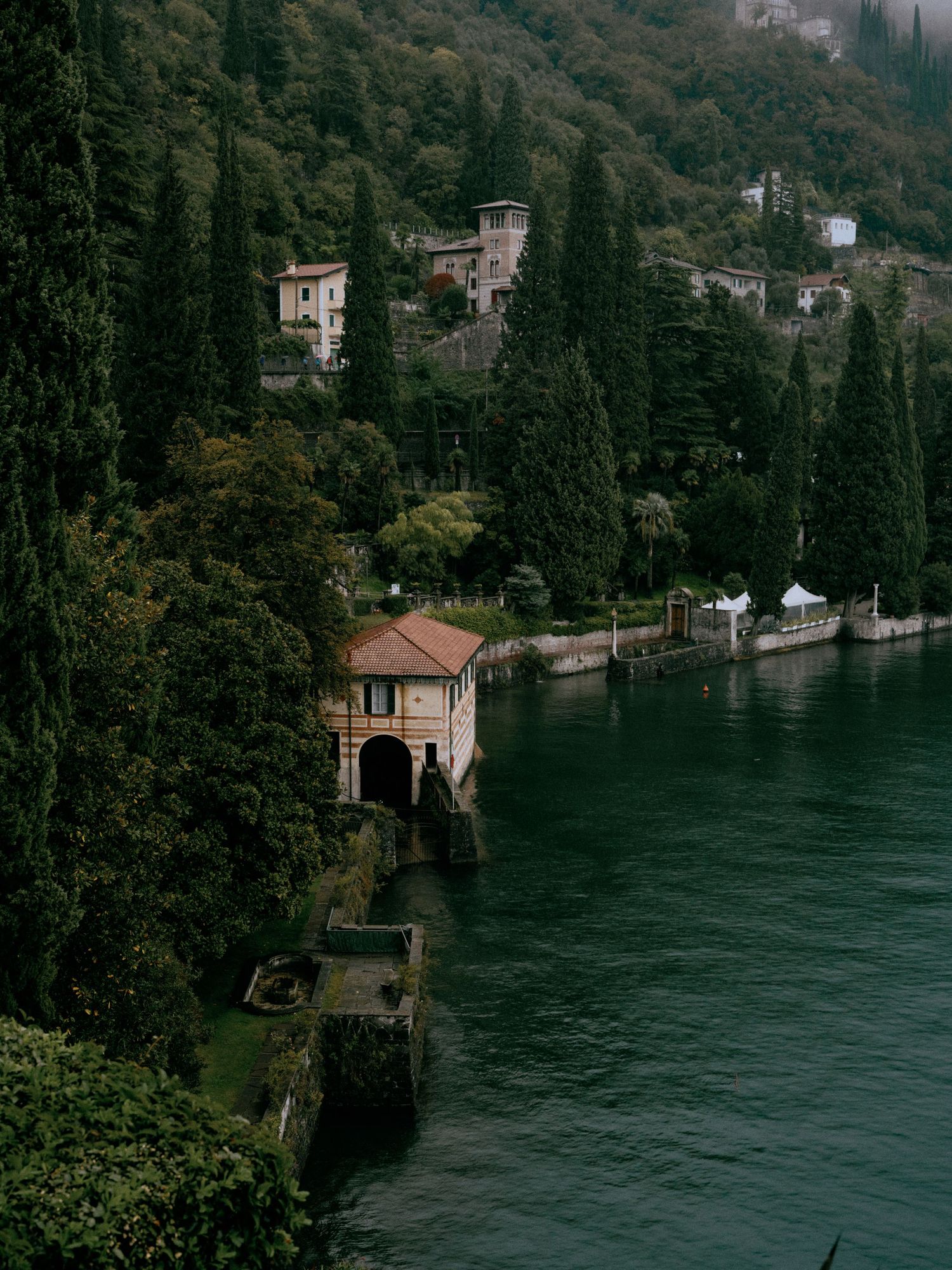 A scenic view of Italian villas nestled among cypress trees along Lake Como's shoreline.
