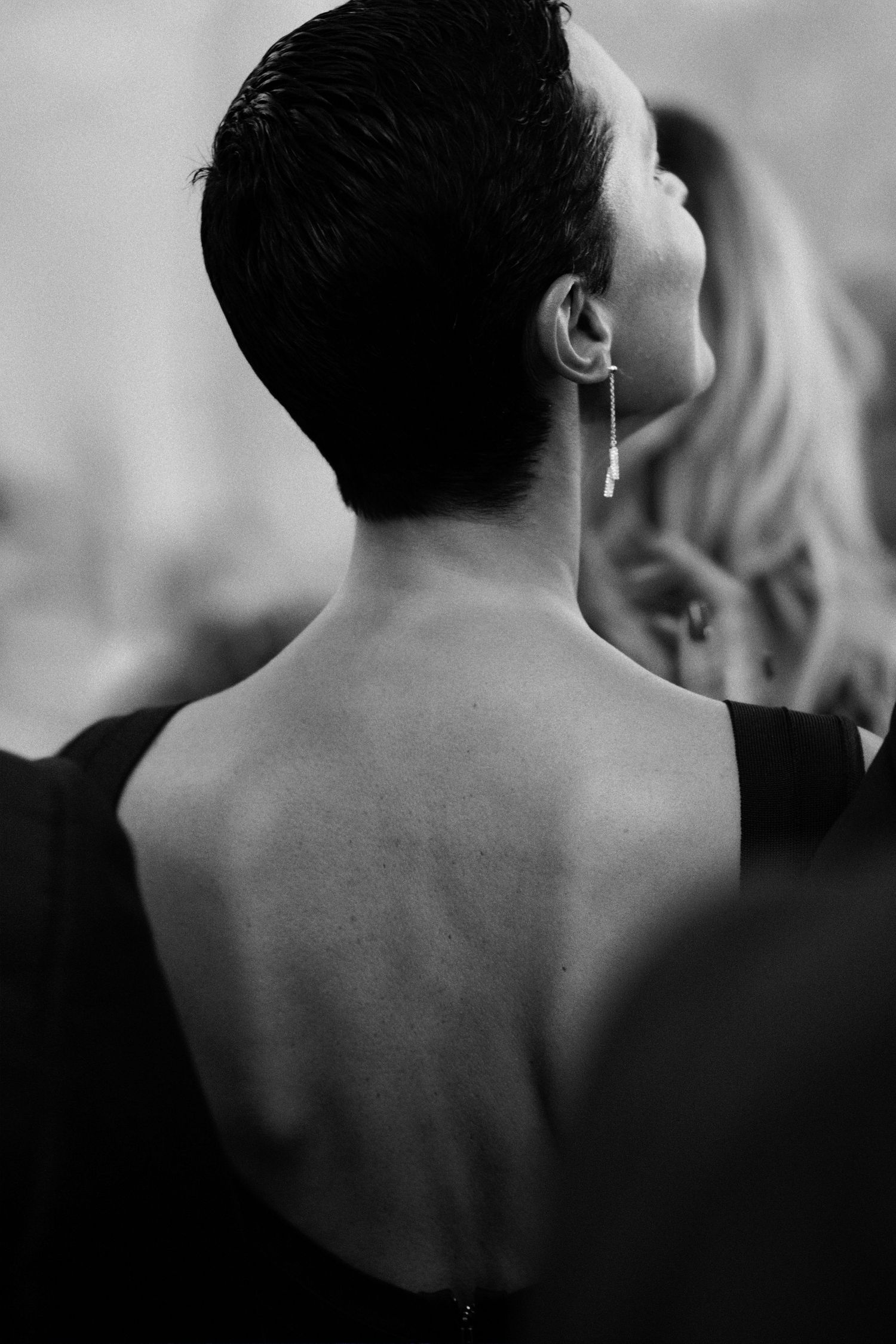 Artistic black and white photo showing the bare back and dangling earring of someone in formal attire.