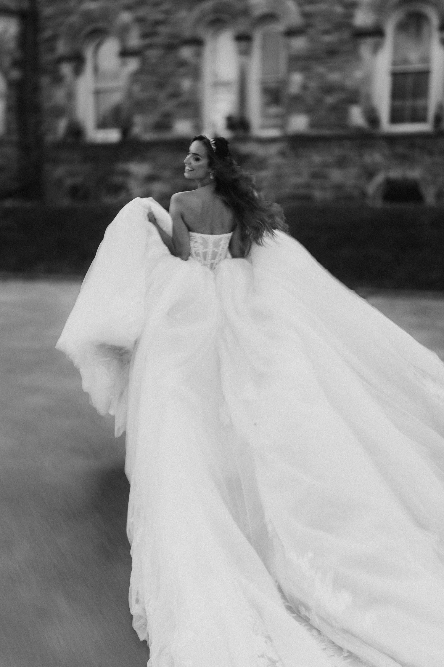 Black and white photo of a flowing wedding dress captured in motion against stone architecture.
