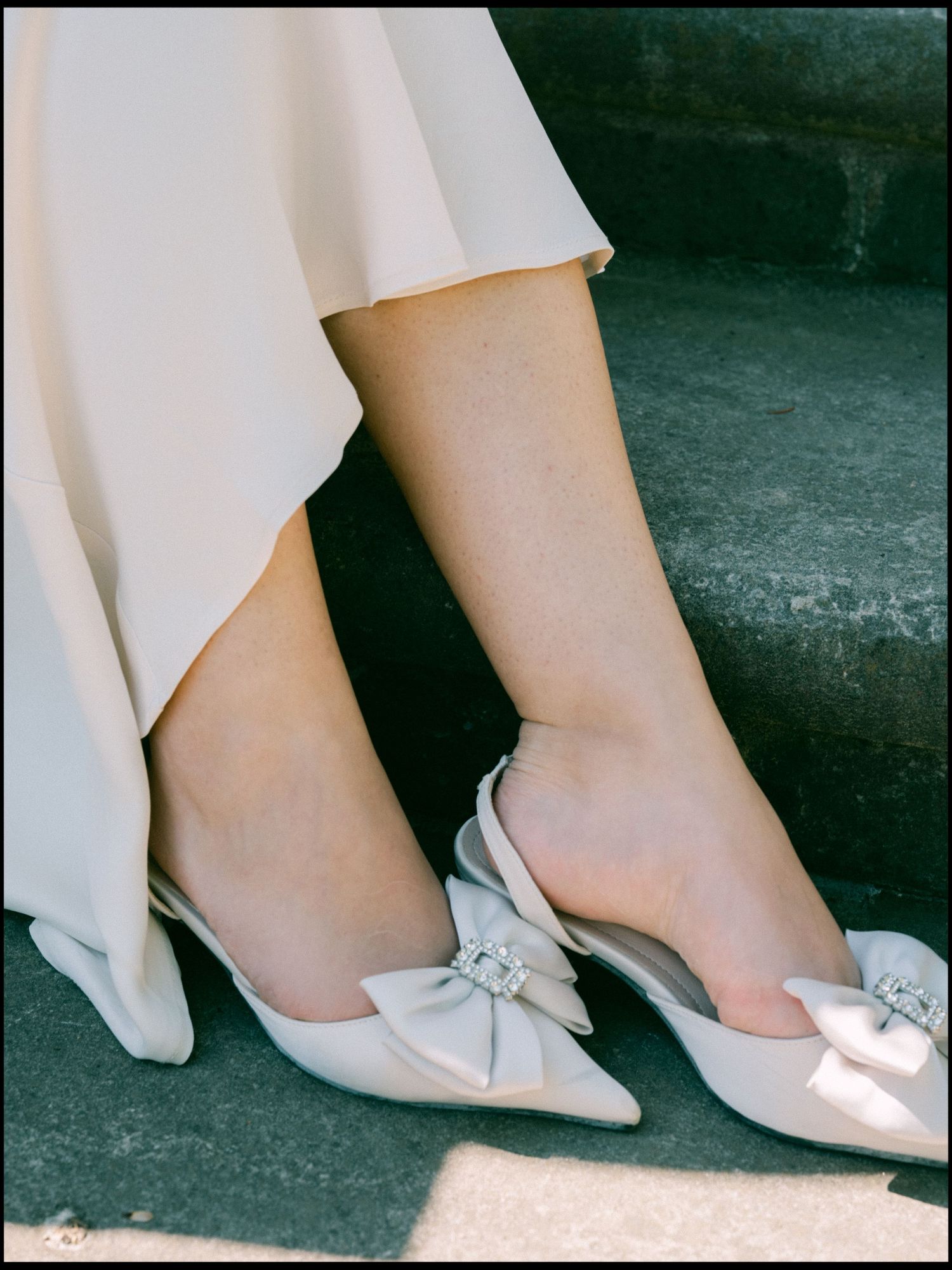 Elegant white satin mules with decorative bow details photographed against a dark background.