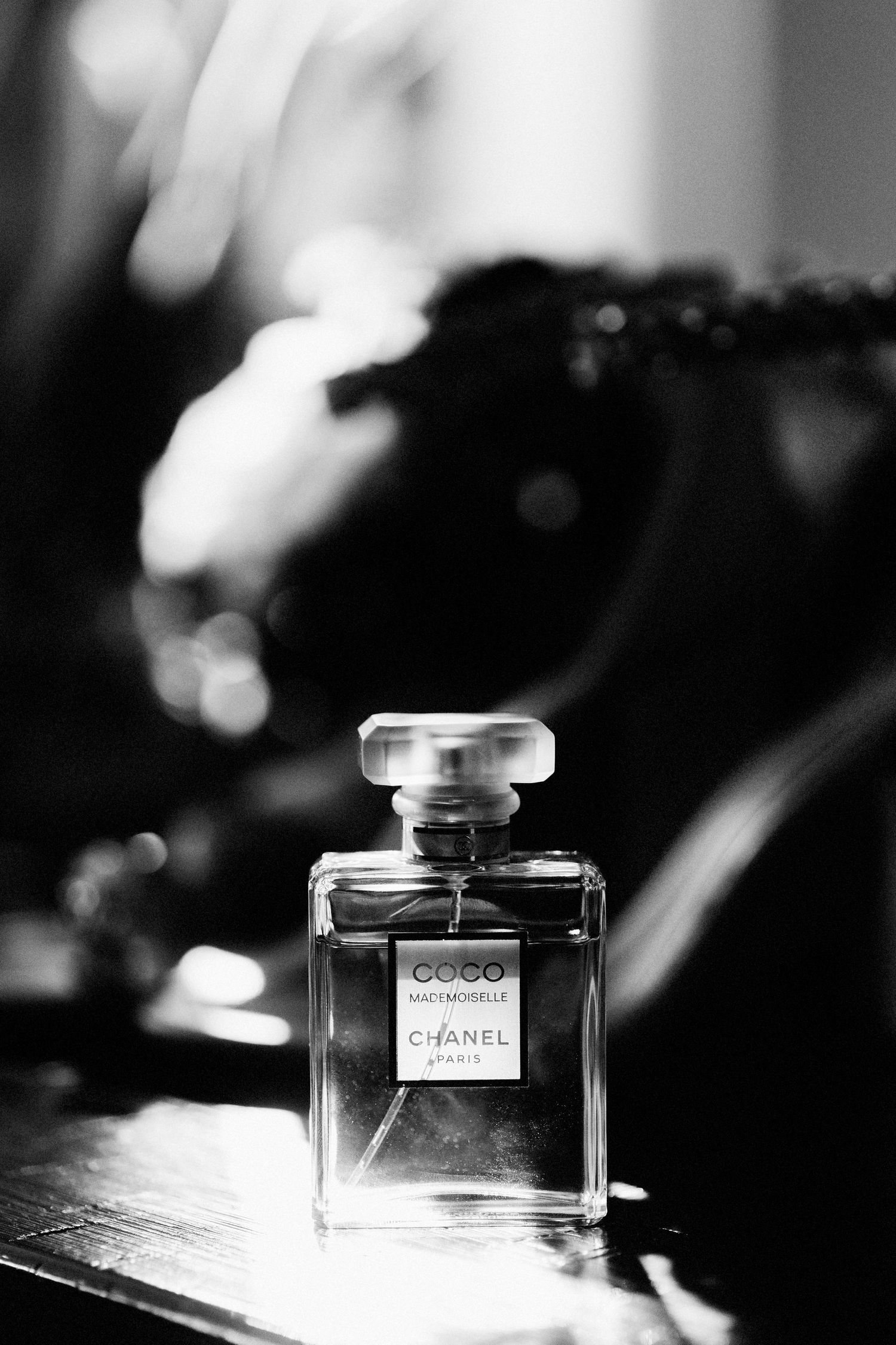 Black and white close-up of a classic Chanel perfume bottle on a reflective surface.
