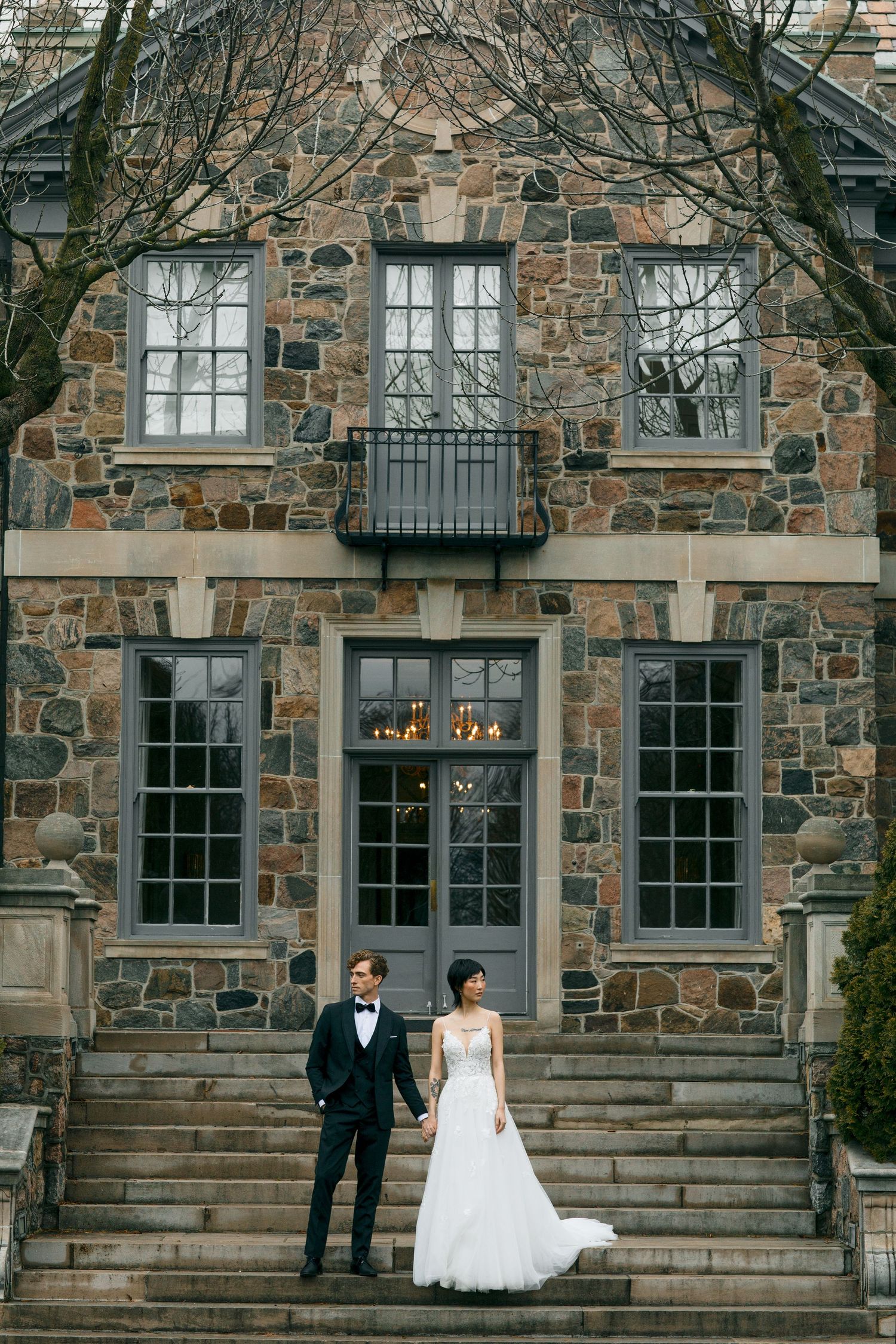 Newlyweds posing on stone steps of historic building with symmetrical windows.