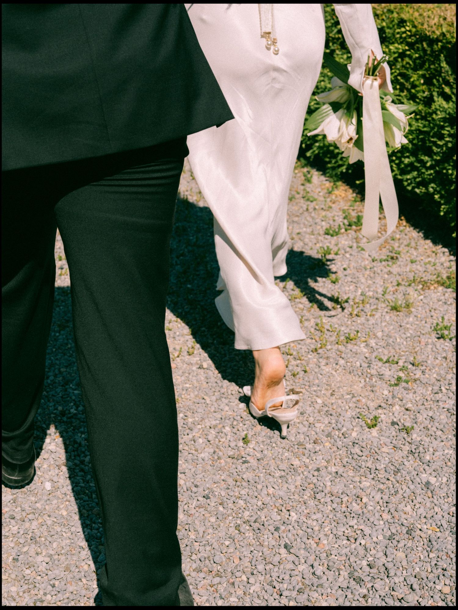 Close-up of wedding couple's feet as they dance on gravel, showing dress and suit details.