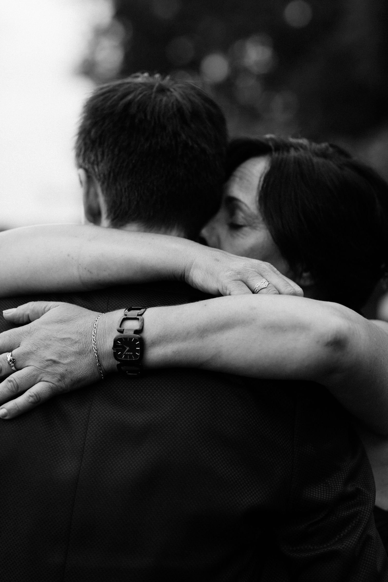 An intimate black and white wedding photo capturing a close embrace with hands and rings visible.