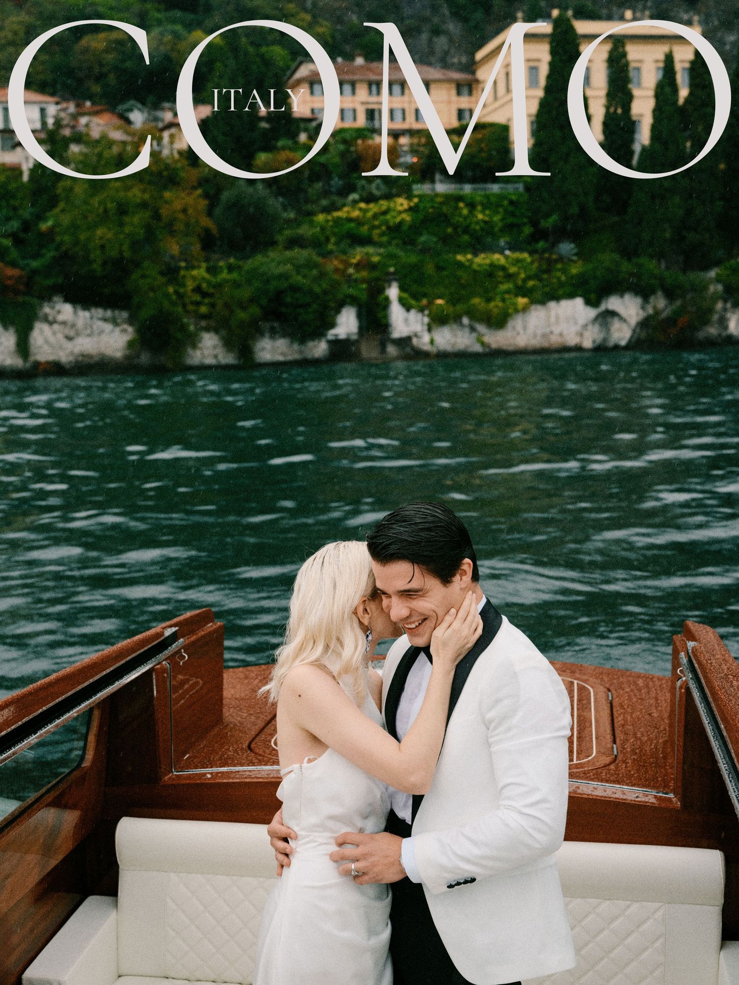 A couple share a romantic moment on a wooden boat on Lake Como, Italy with mountains and greenery in the background.