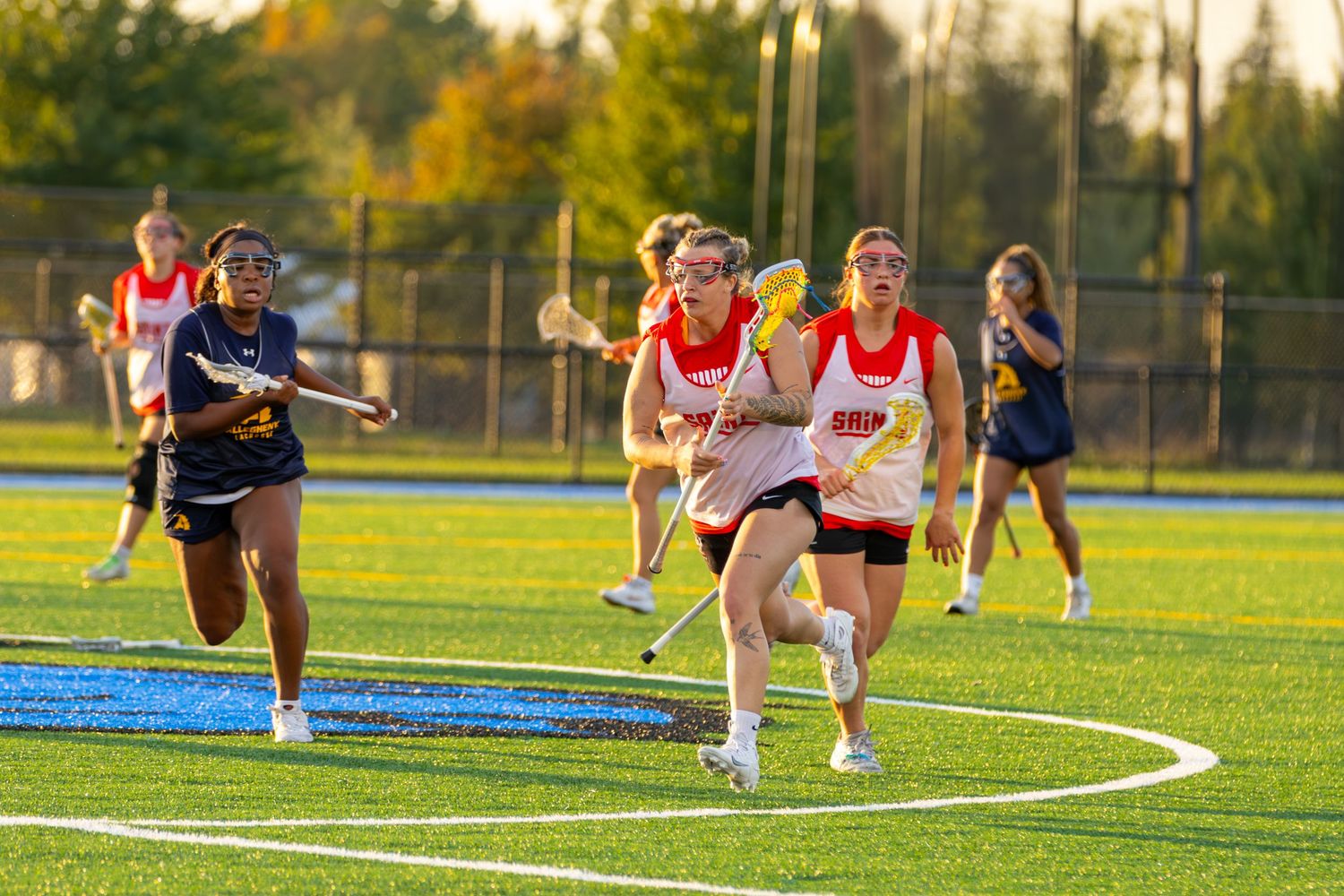 Athletes stretch and warm up on a sports field during golden hour sunset with autumn trees in the background.
