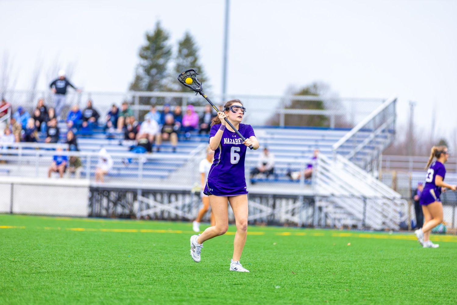 Female lacrosse player wearing purple jersey number 6 running on field during a competitive game.
