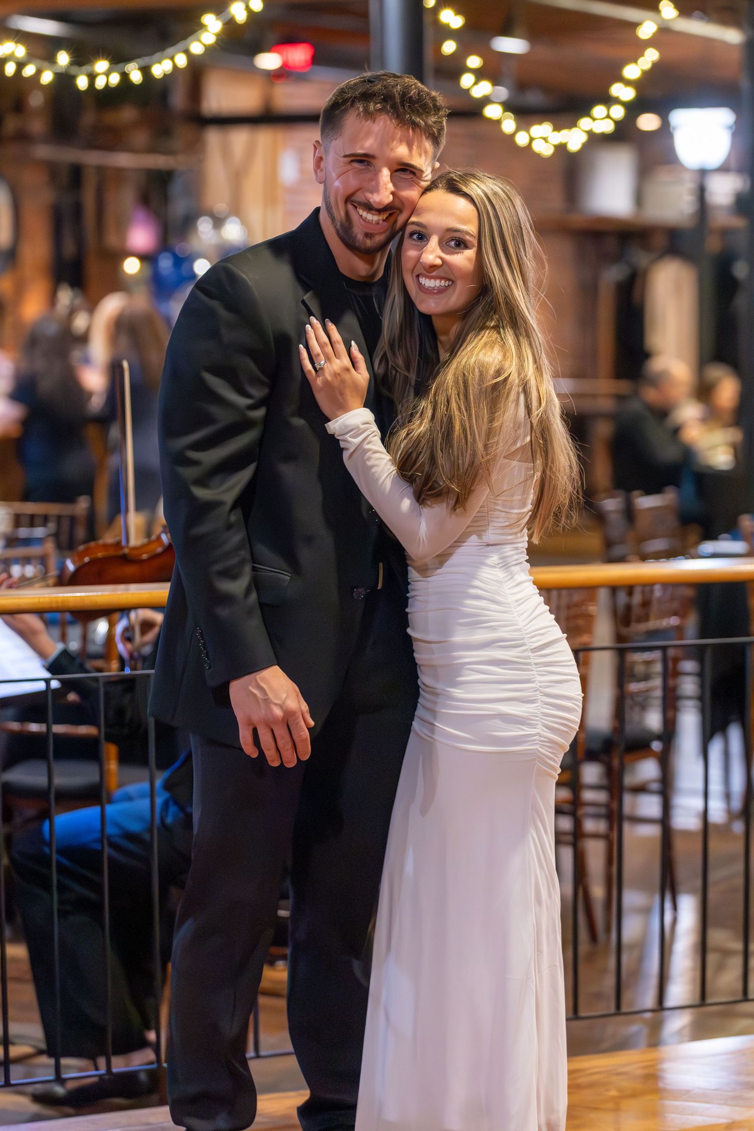 A couple shares a romantic moment on the dance floor at a wedding reception with twinkling lights in the background.