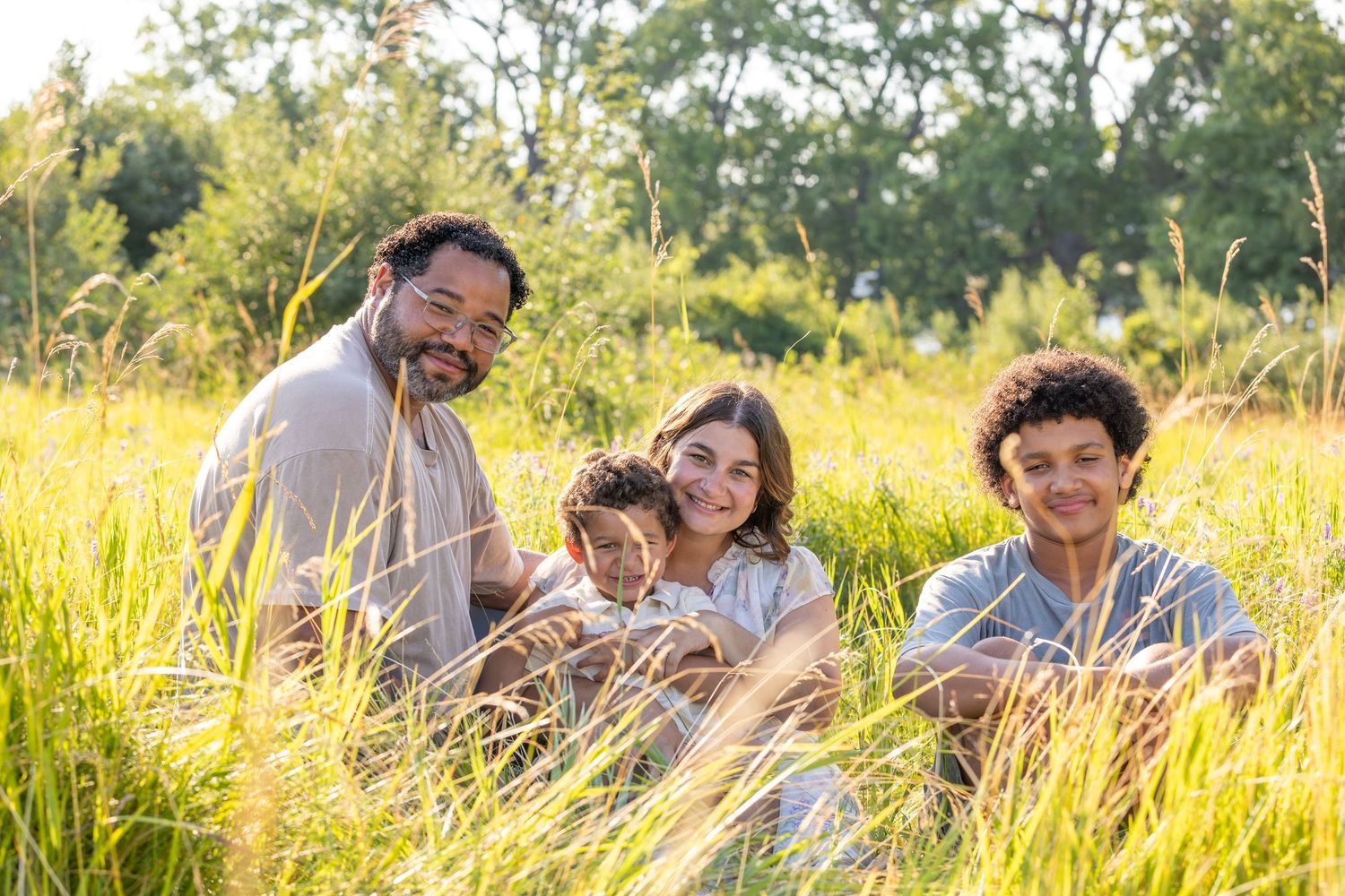 Family enjoying a candid moment together while sitting in a sun-drenched meadow during golden hour.