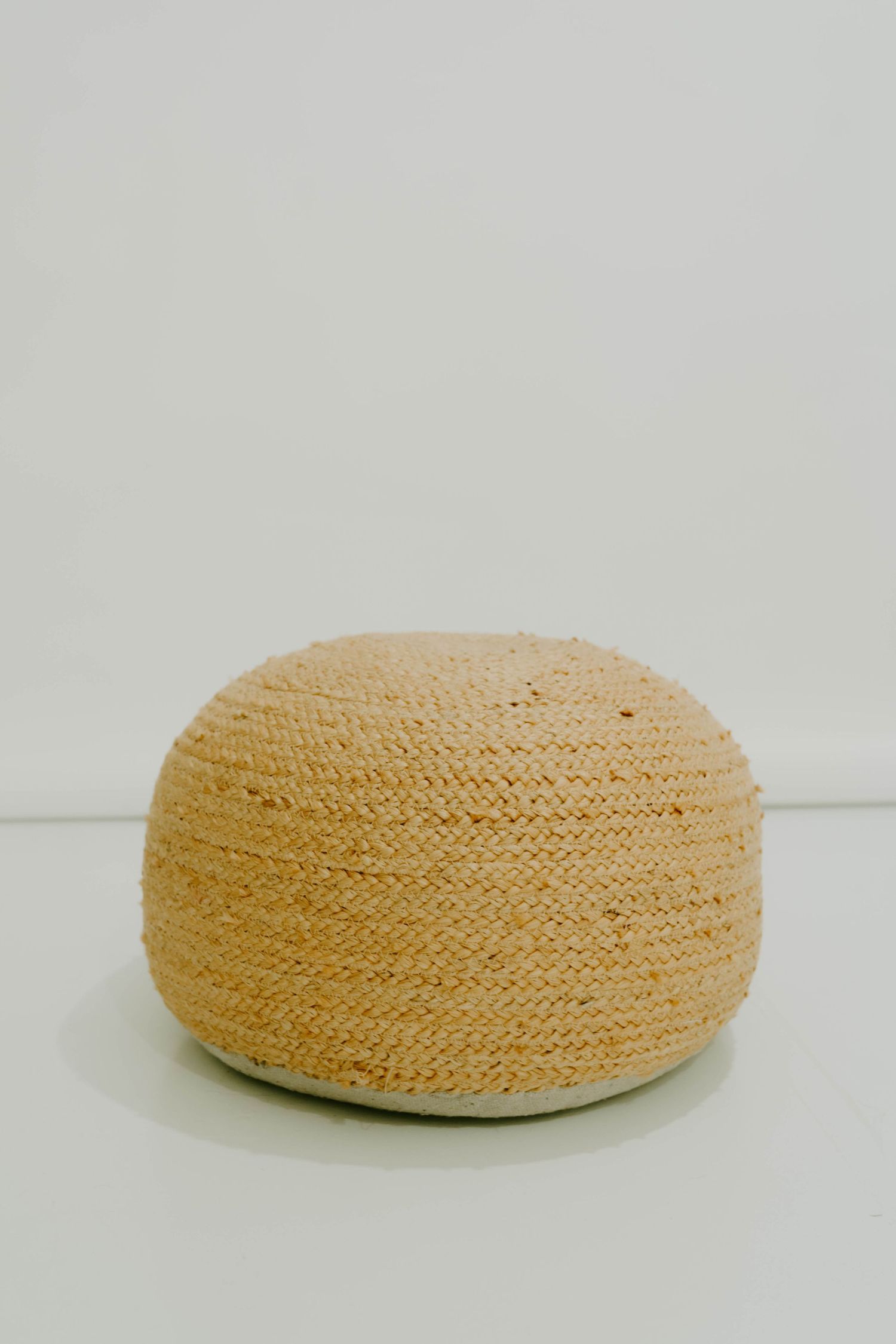 Round woven natural fiber cushion or pouf photographed against white background.