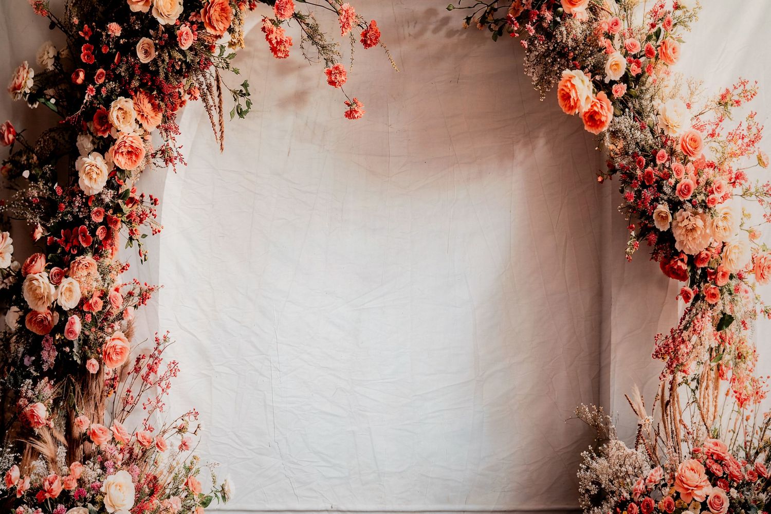 Romantic floral arch with coral and peach roses against a white backdrop.