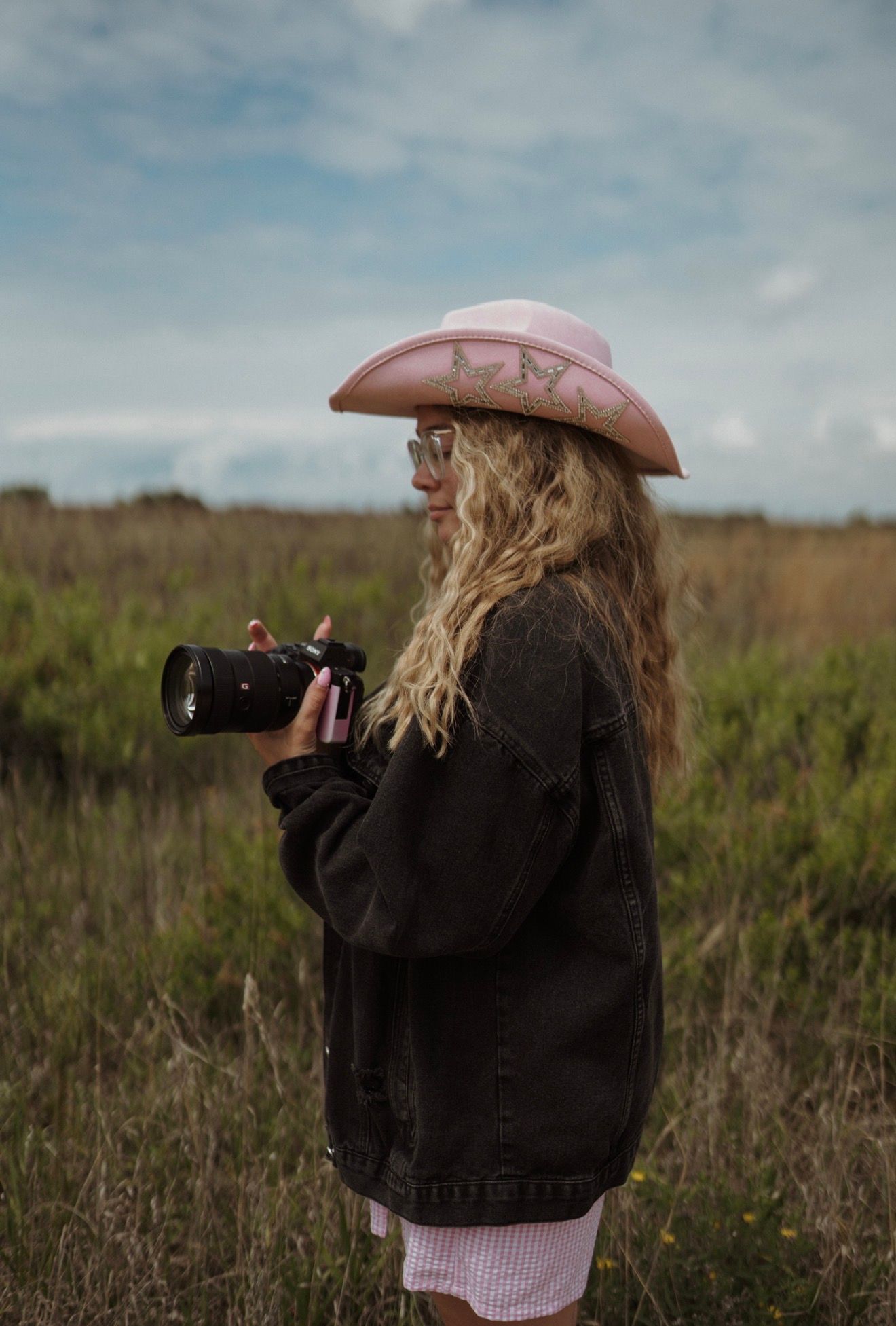 Photographer wearing pink cowboy hat shooting in grassy field.