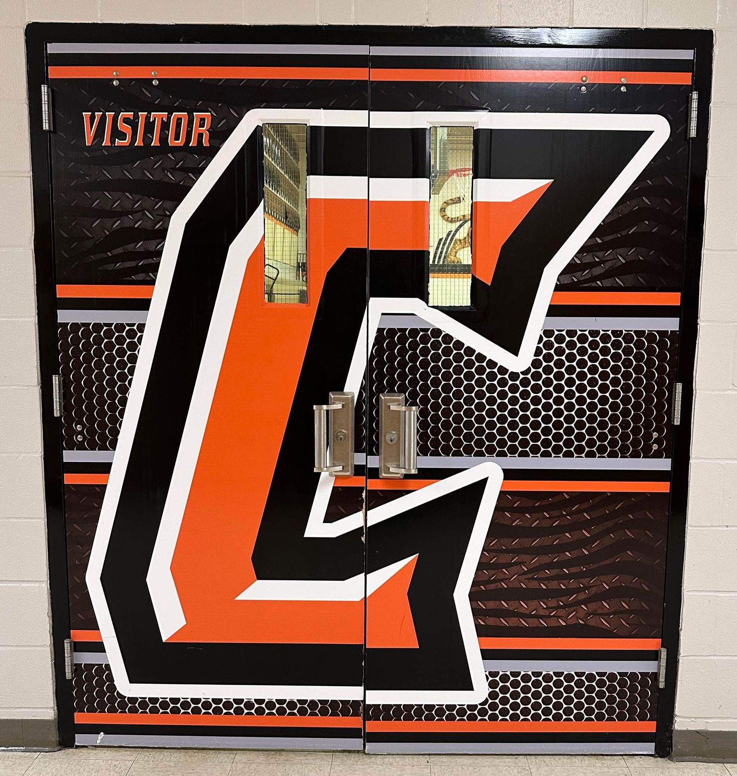 Orange and black sports team locker decorated with large letter C design and visitor sign in mesh-style backdrop.