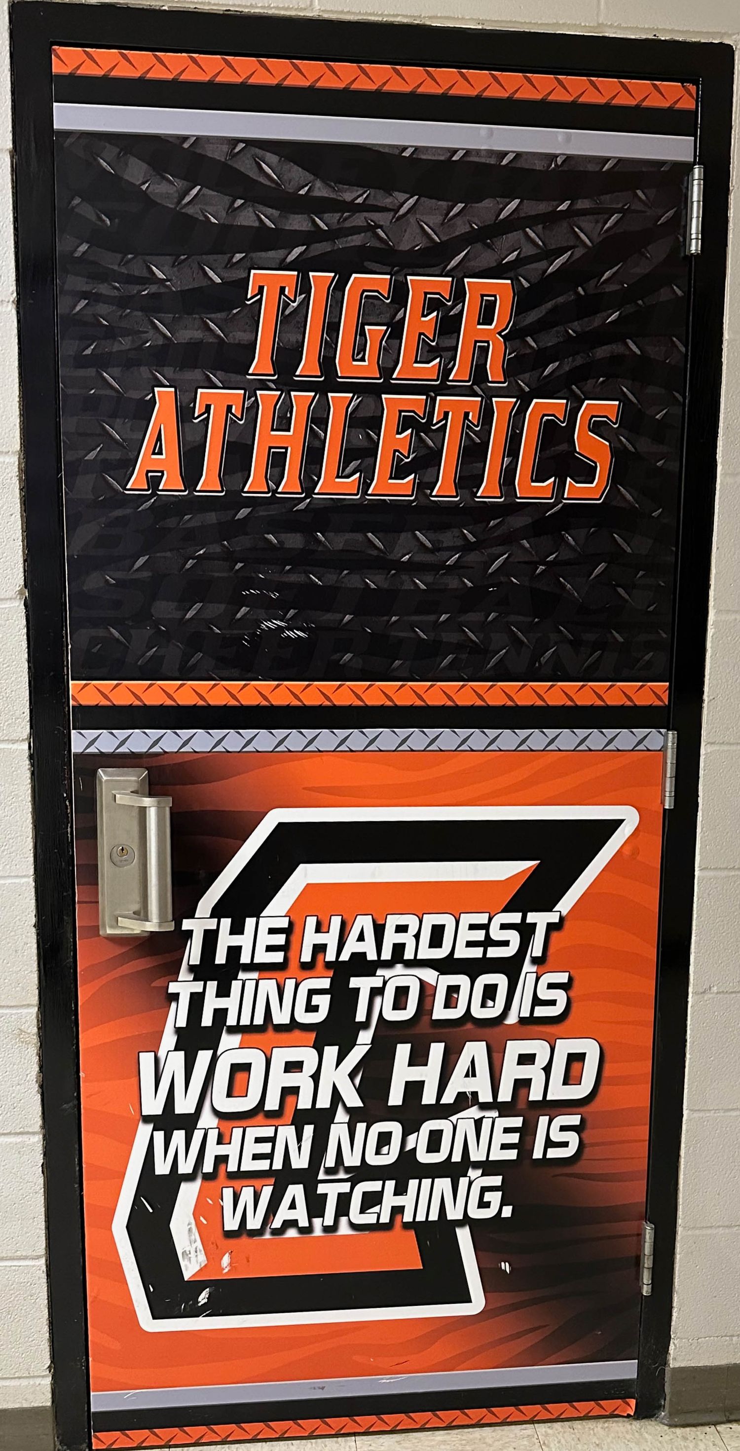 School athletic facility door displays Tiger Athletics logo and motivational quote about working hard in black and orange colors.