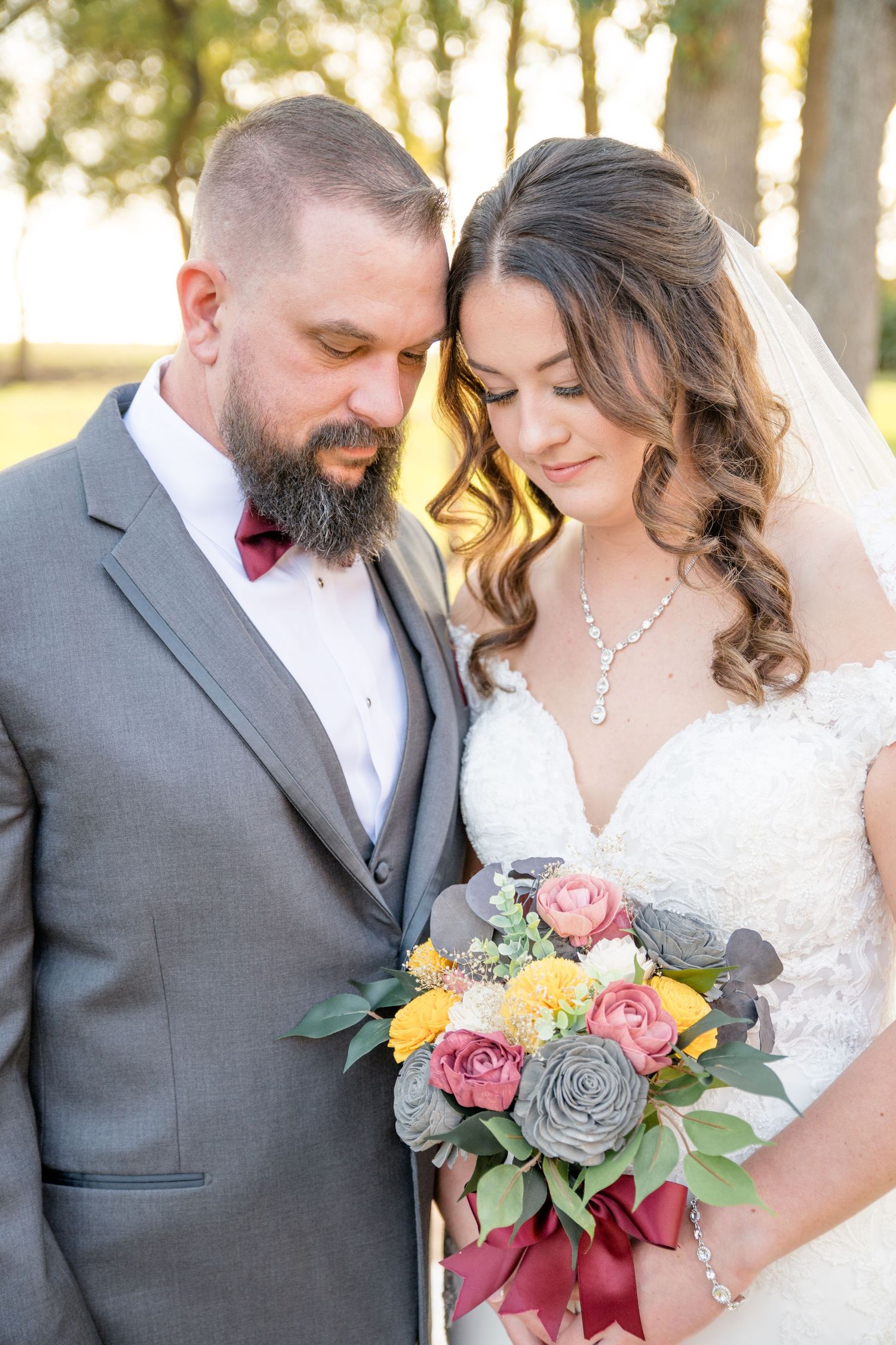 A romantic wedding couple poses together outdoors while holding a beautiful bouquet with pink and yellow roses.