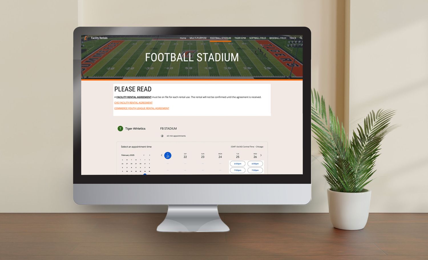 A computer monitor displaying a football stadium seat reservation interface with a potted plant beside it on a wooden desk.