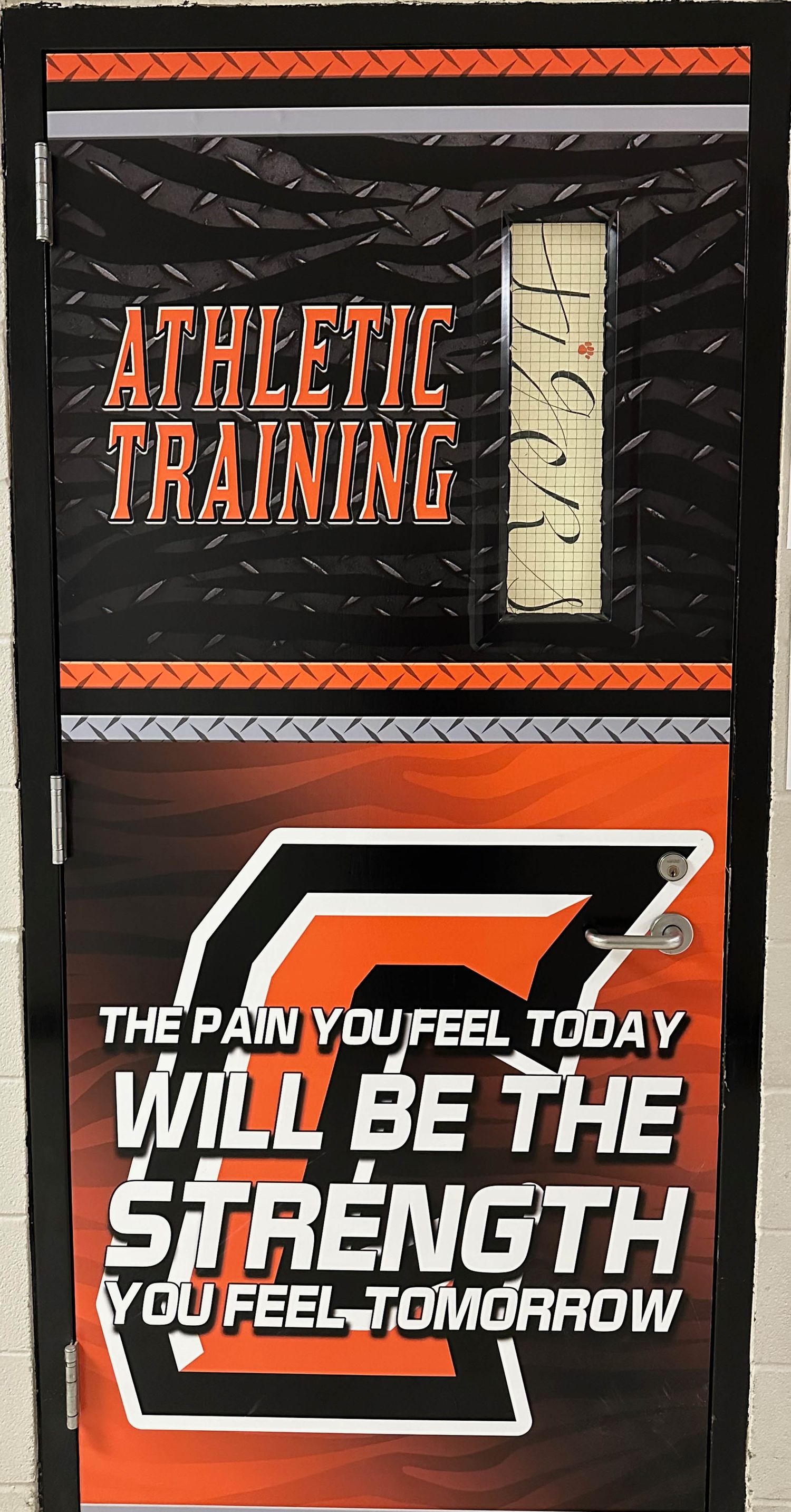 Athletic training room door with orange and black design featuring motivational quote about pain and strength.