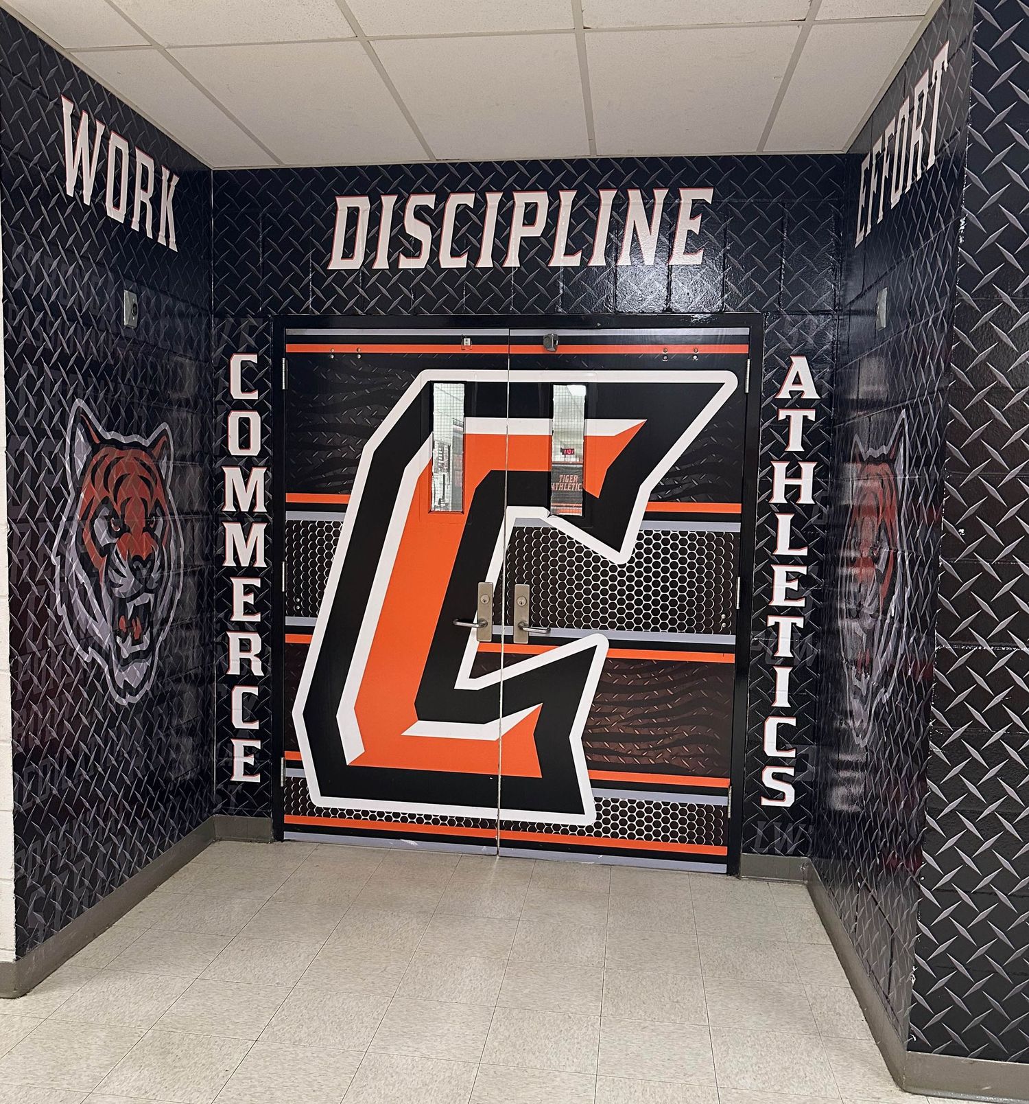 Gym hallway with black walls displaying 'DISCIPLINE' text and orange athletic logo between 'COMMERCE' and 'ATHLETICS' signage.