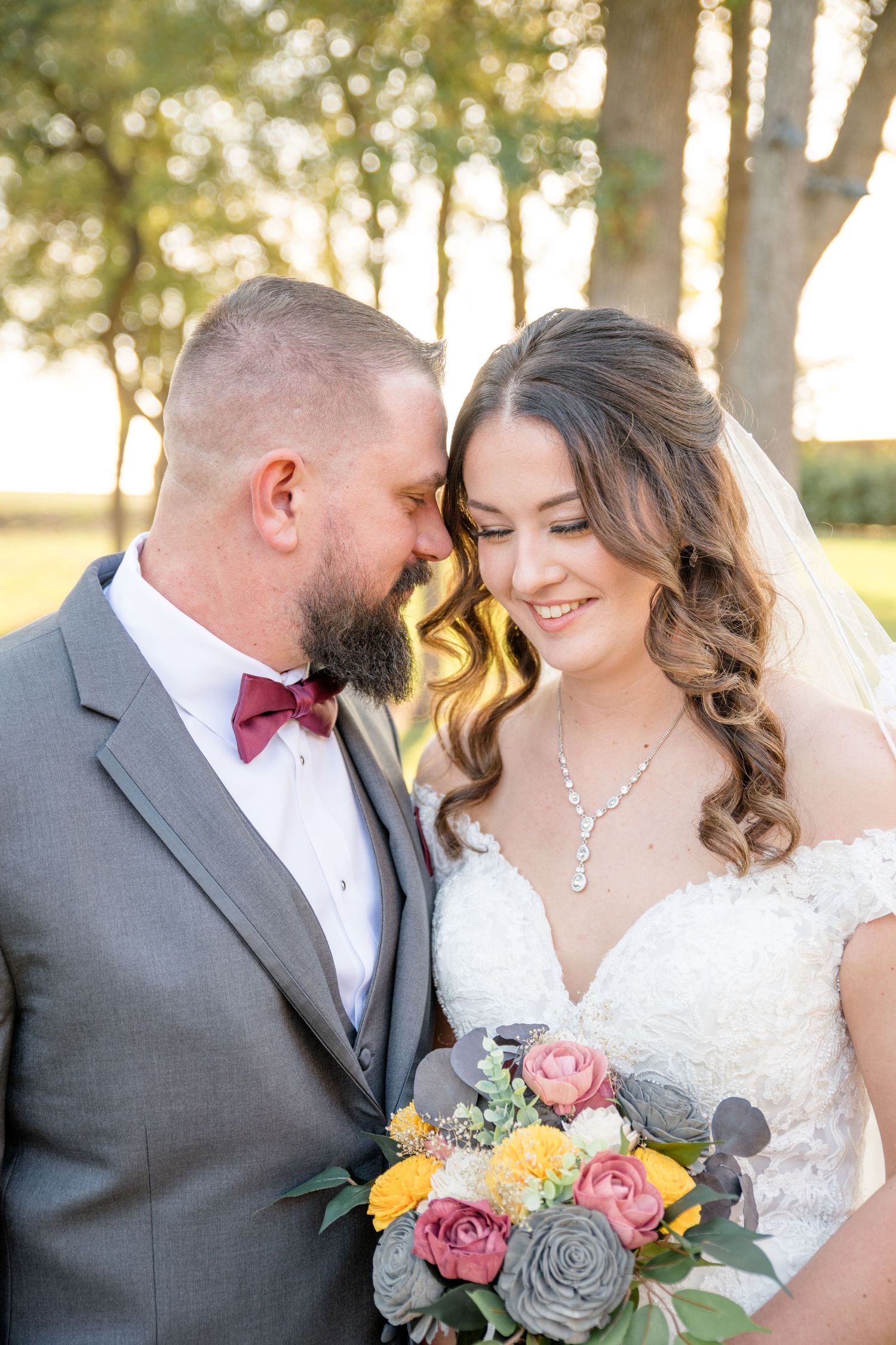 A romantic outdoor wedding portrait featuring a couple in formal attire with a colorful bouquet of roses and eucalyptus.