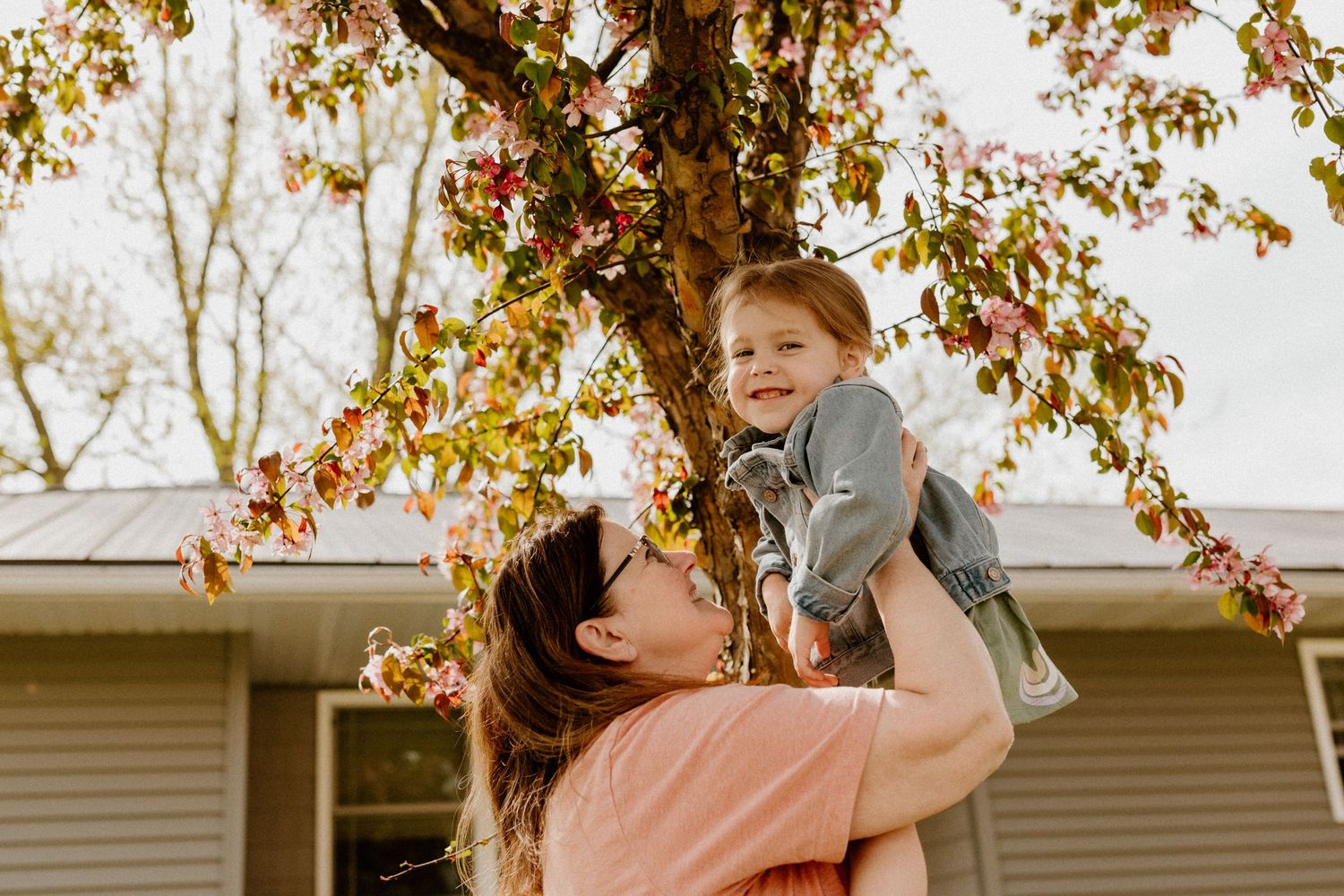 A joyful autumn moment captured in golden sunlight as parent lifts child high beneath colorful falling leaves.
