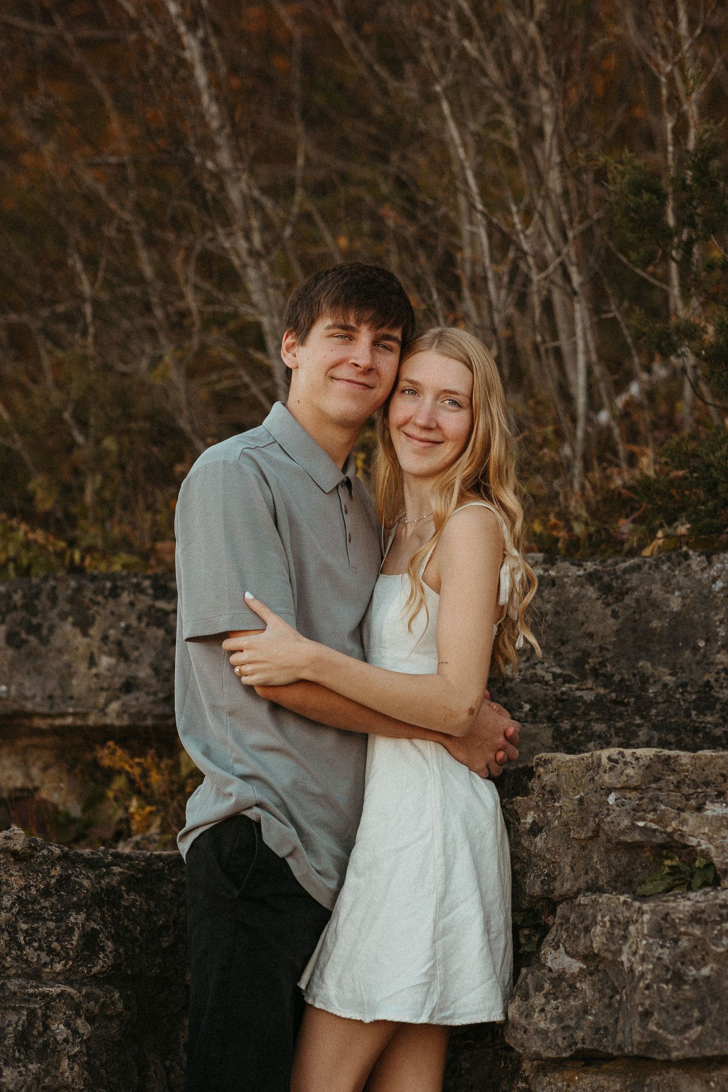 A couple embraces against a stone wall during an autumn engagement shoot.