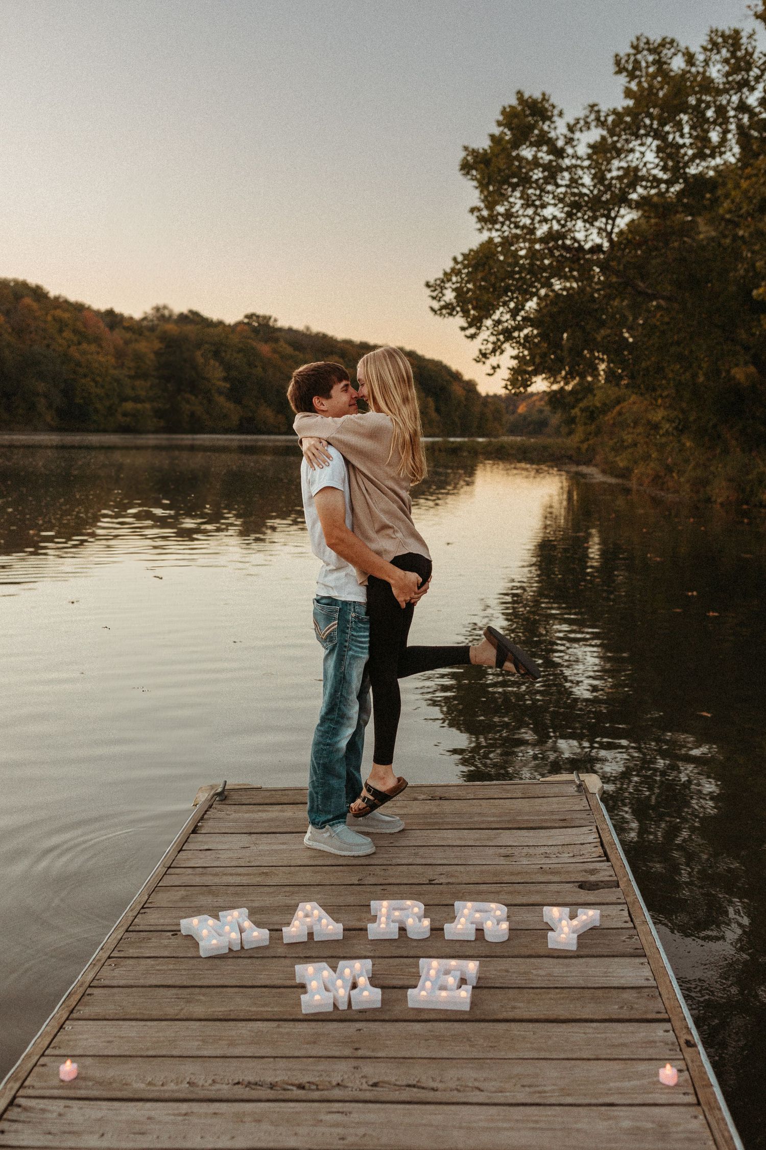 A romantic dock proposal with 'MARRY ME' spelled out in letters at sunset.