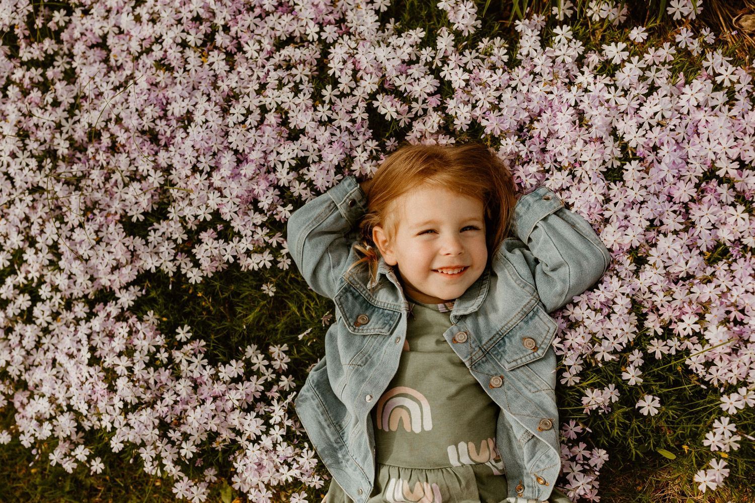 A cheerful child lying among pink spring blossoms wearing a denim jacket.