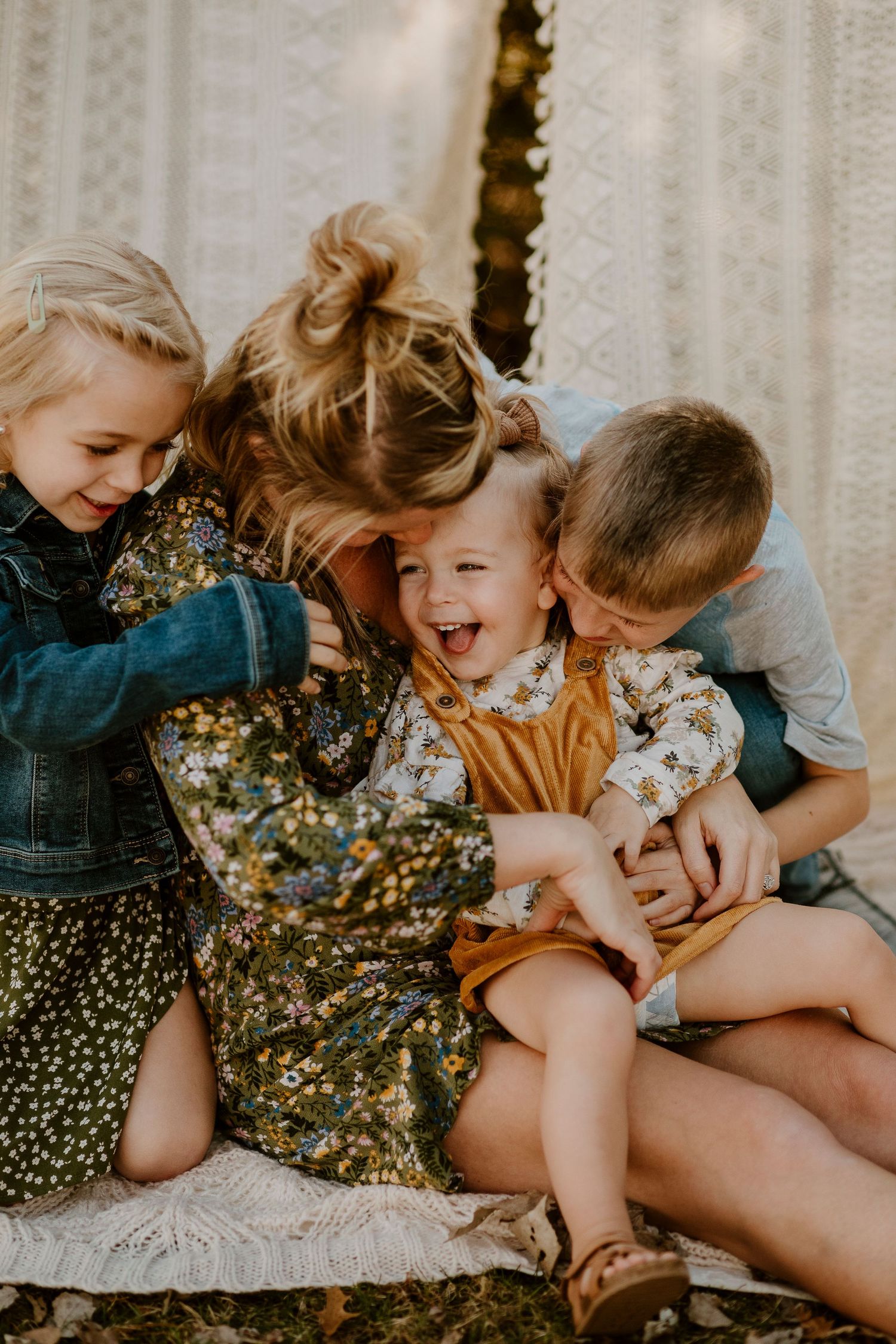 Children share a joyful moment of laughter and tickles together on a white blanket.