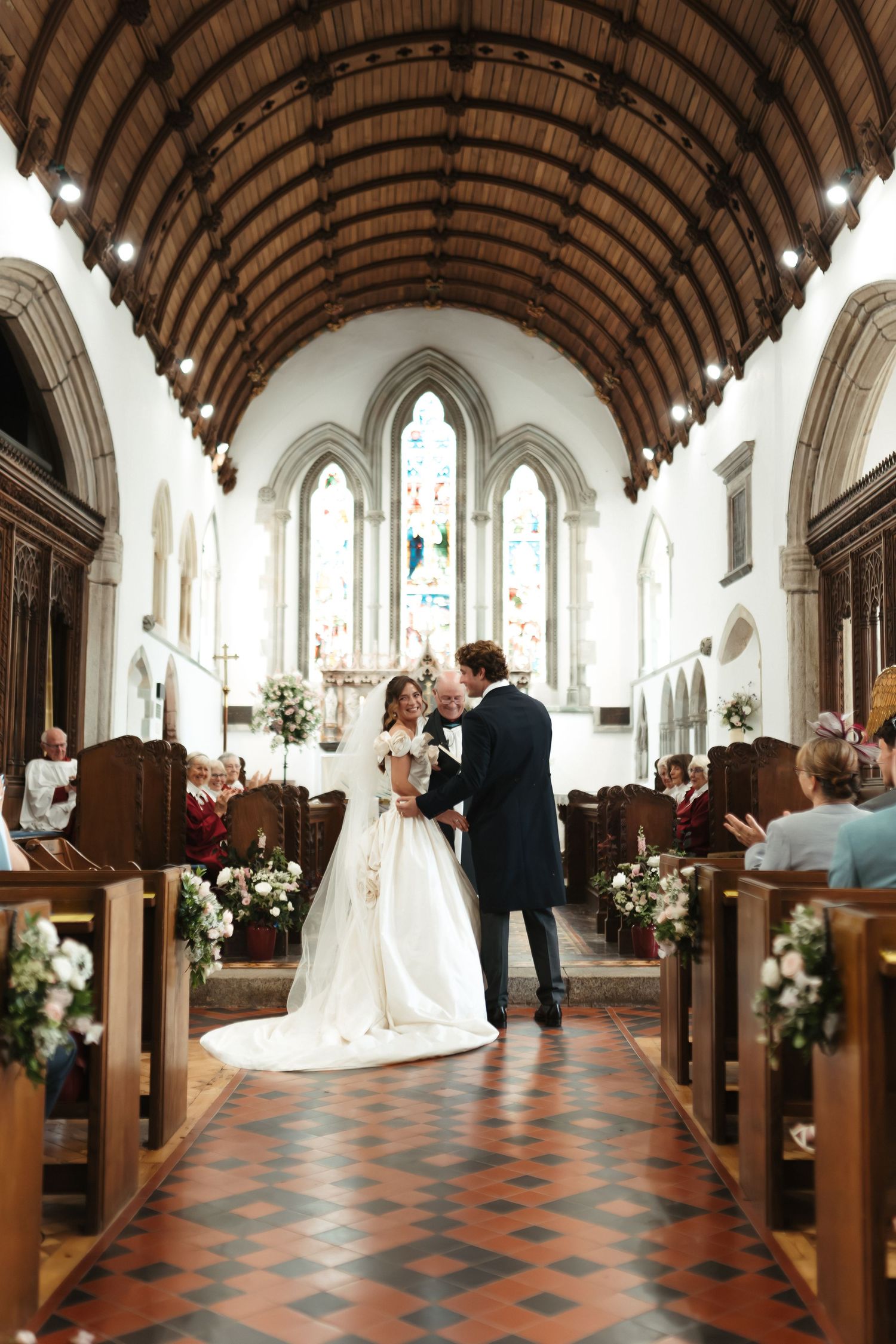 Bride and groom share a kiss at the altar of a stunning Gothic church with wooden pews and stained glass windows.