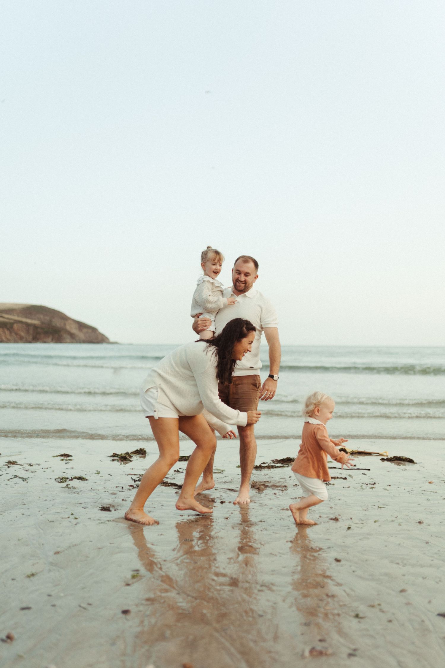 People playing and laughing together on a sandy beach during a cloudy day near the ocean.