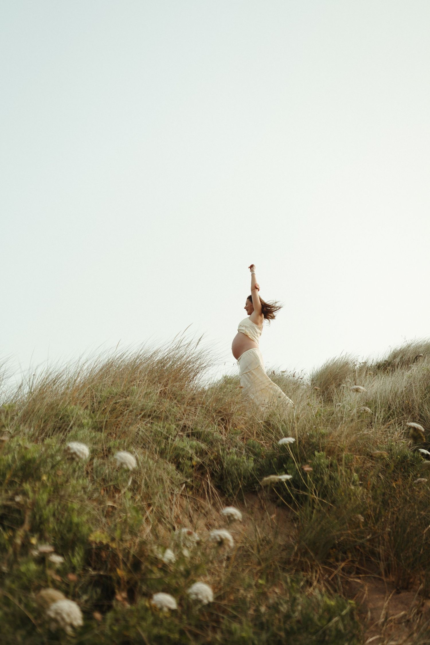 A whimsical figure stands silhouetted against the sky atop a grassy hill, surrounded by swaying coastal vegetation.