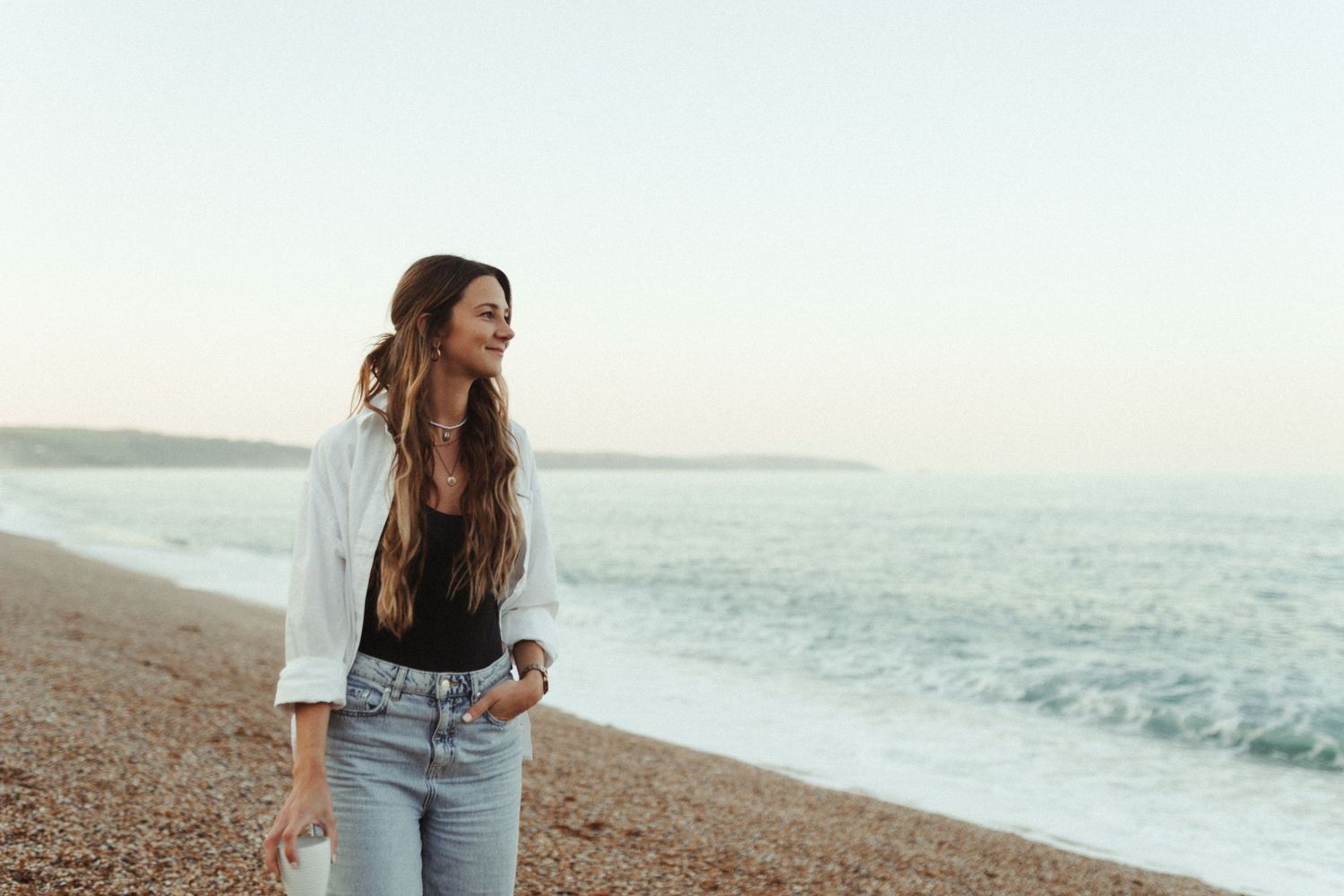A person walks along a dramatic coastal beach at sunset with waves crashing against the shore.