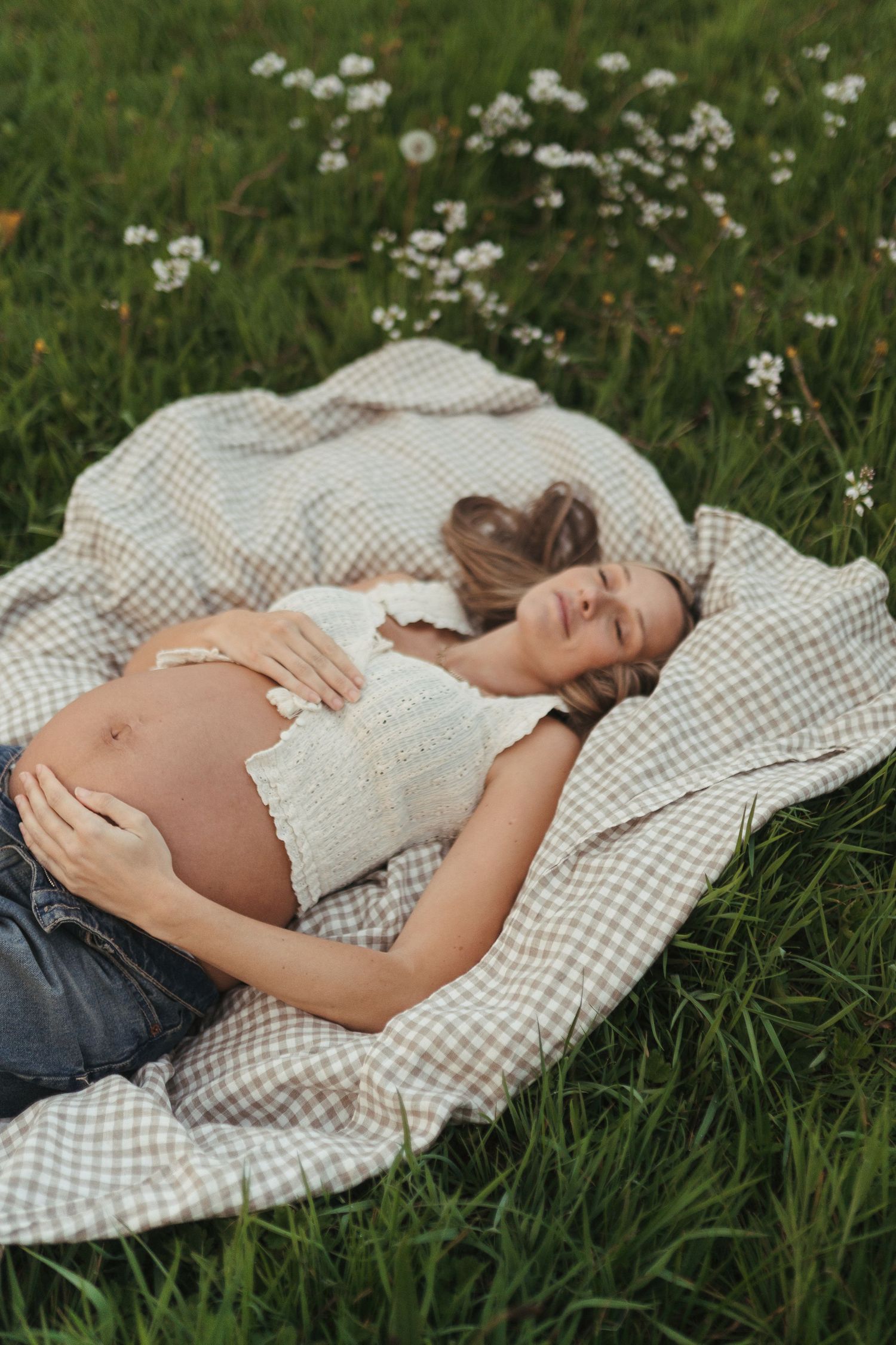 A set of progressive maternity photos showing a pregnant woman resting on a gingham blanket among wildflowers.
