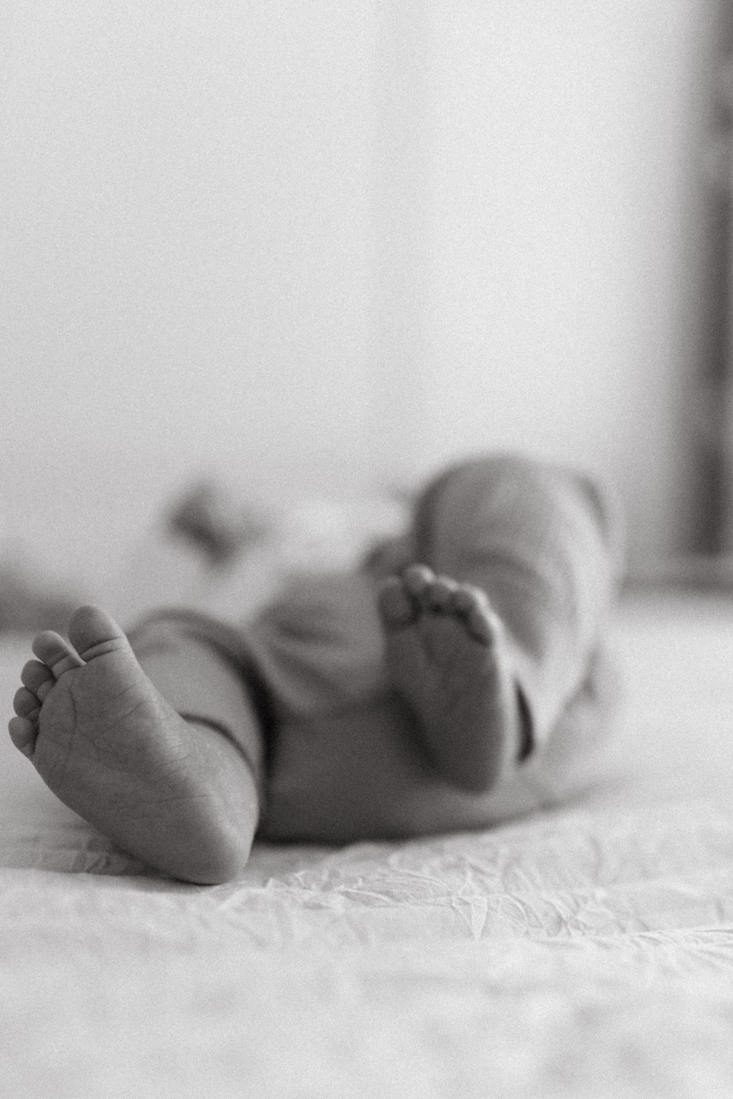 Tiny baby feet in black and white closeup photo lying on soft white textured fabric.