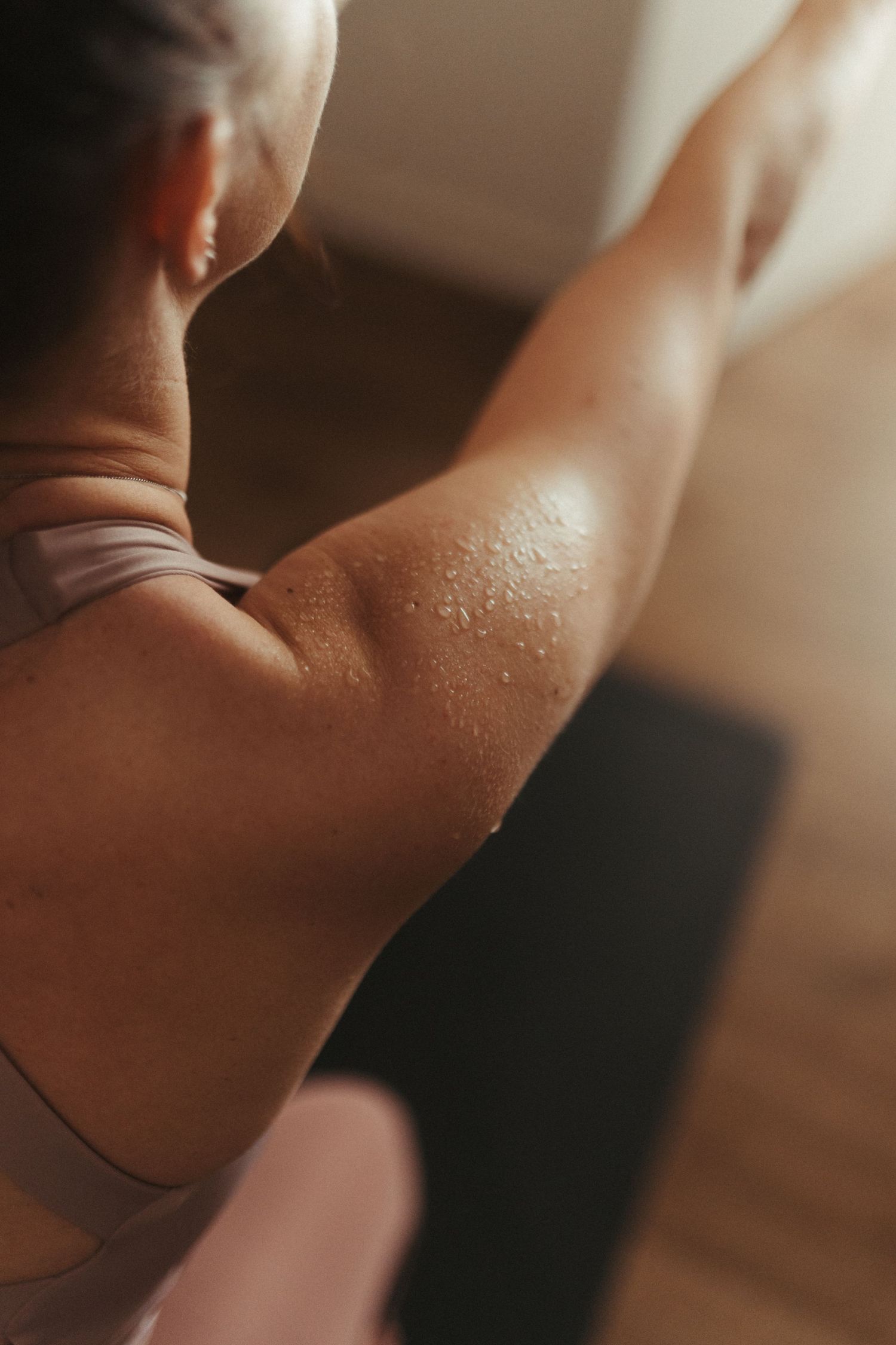Close-up of a sweaty athletic arm and shoulder during an intense workout session on a wooden floor.