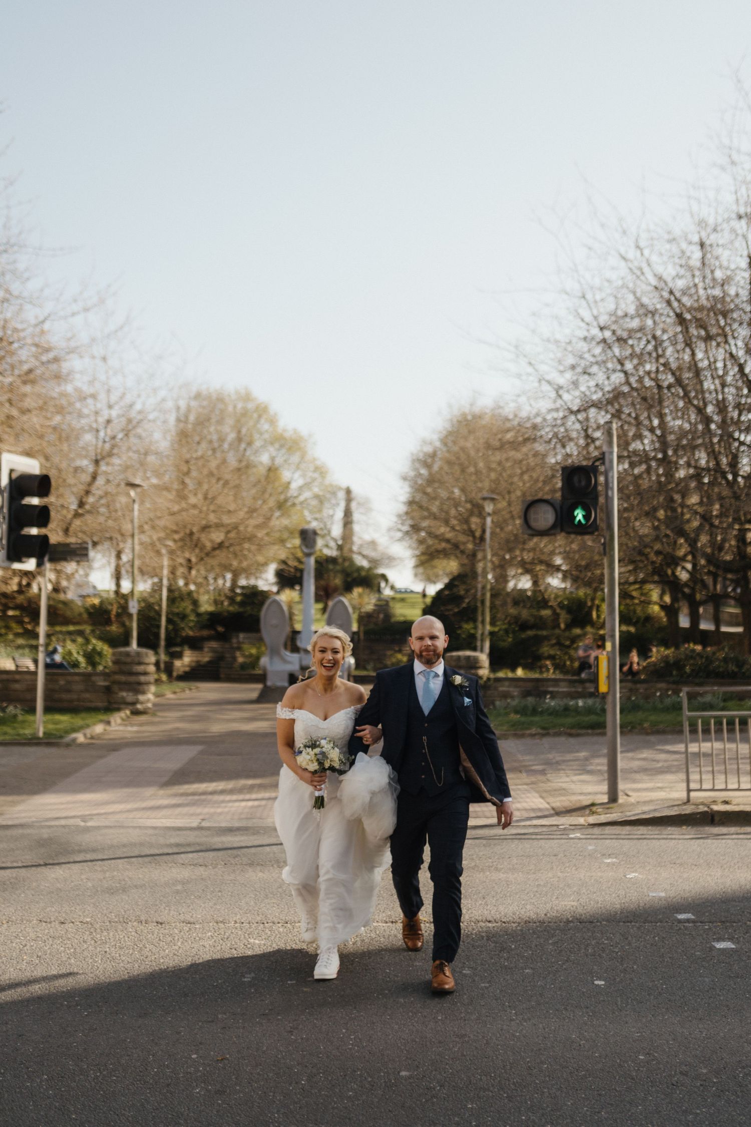 A couple walks together on a quiet tree-lined street during their wedding photo session.