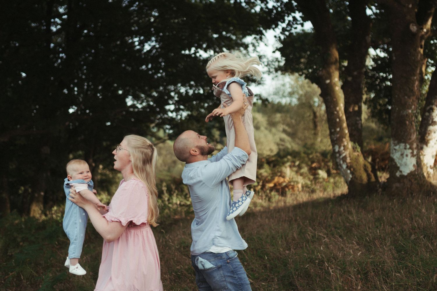 A family enjoys a tender bonding moment together in a sun-dappled forest setting at golden hour.