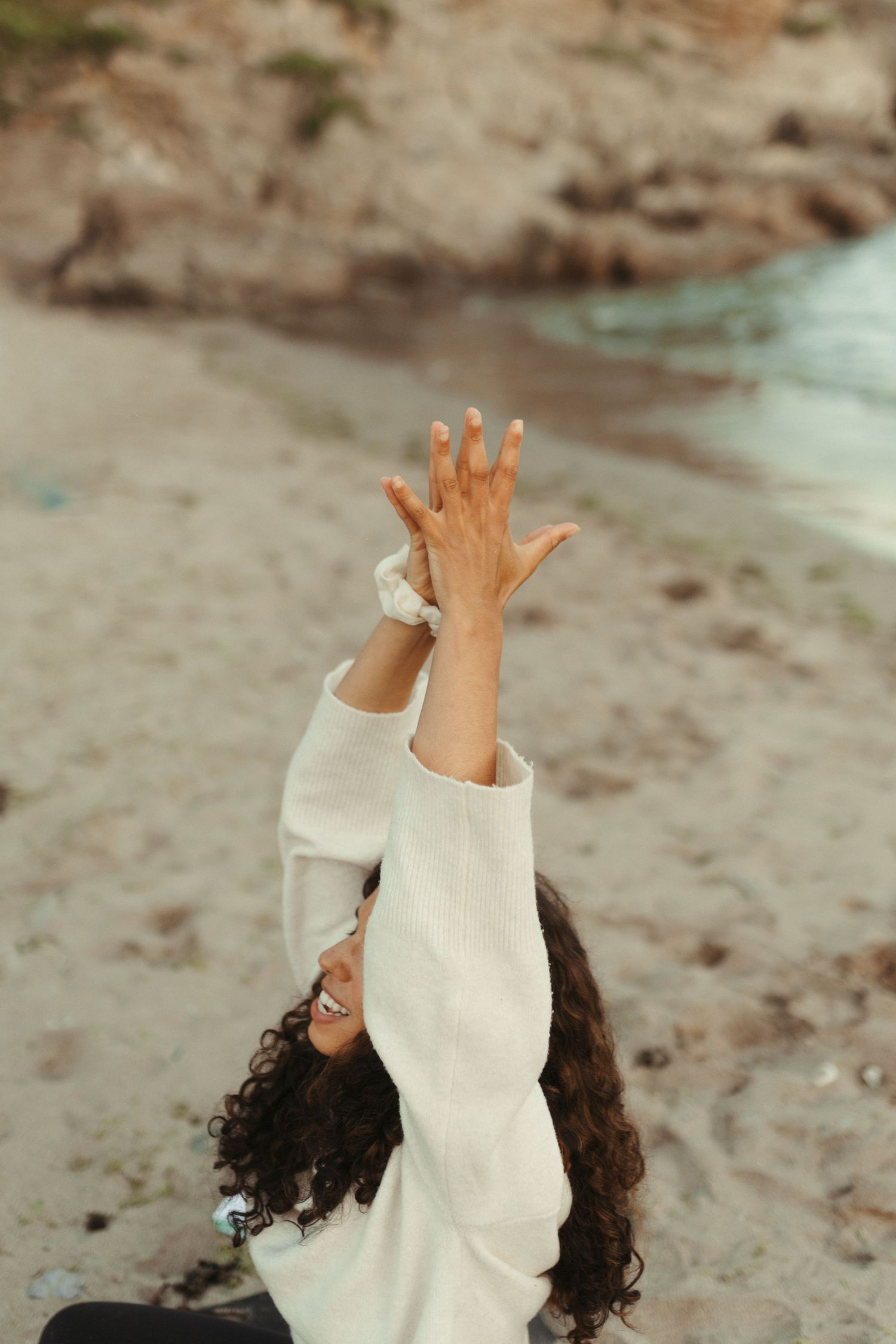 Person in a white sweater lies on ground while expressively gesturing with hands during an artistic performance.