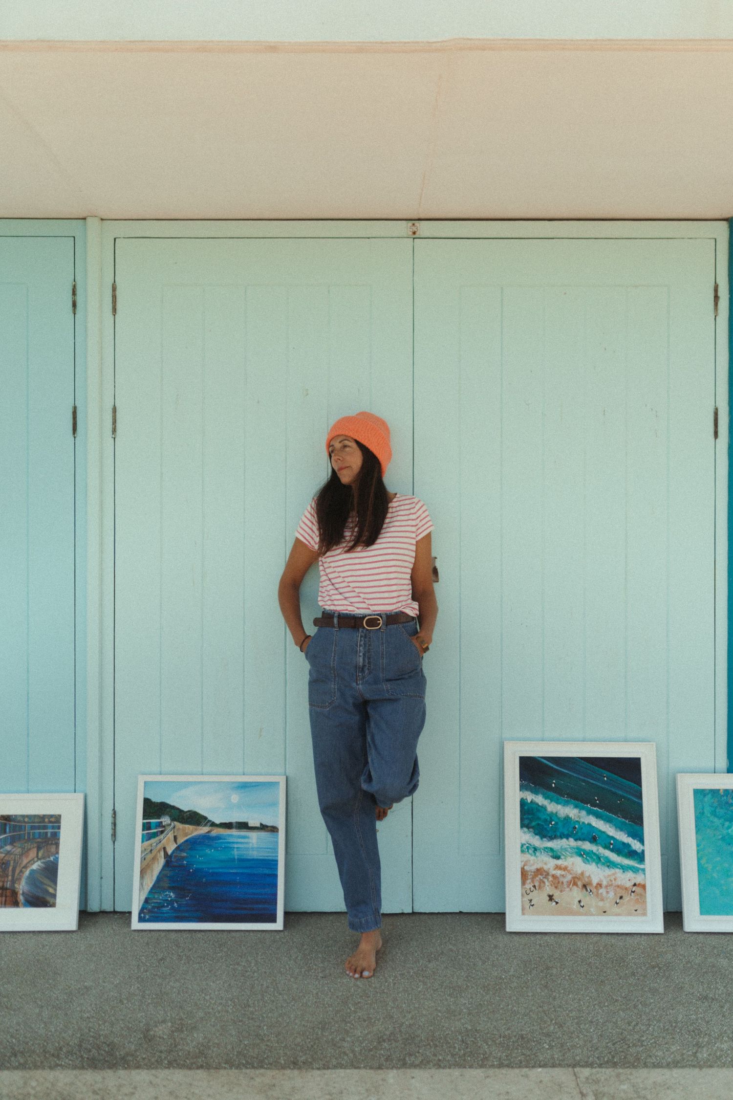 A person in jeans and striped shirt crouches to view ocean photographs displayed along a turquoise wall.