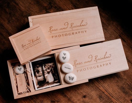 Rustic wooden photography boxes with custom branding and decorative heart-shaped trinkets displayed on dark wood surface.