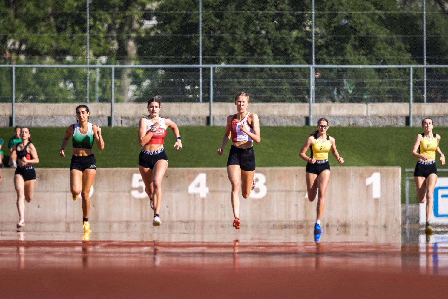 Athletes competing in a track race on an outdoor stadium with numbered lanes during a competition.