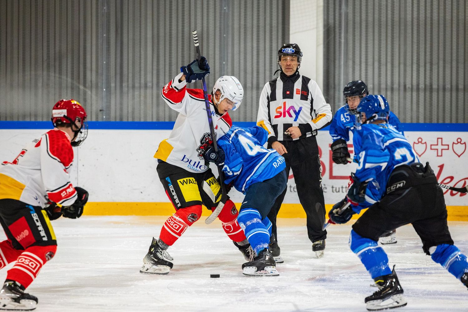 Ice hockey players in red and blue jerseys compete for the puck during an intense match on the rink.