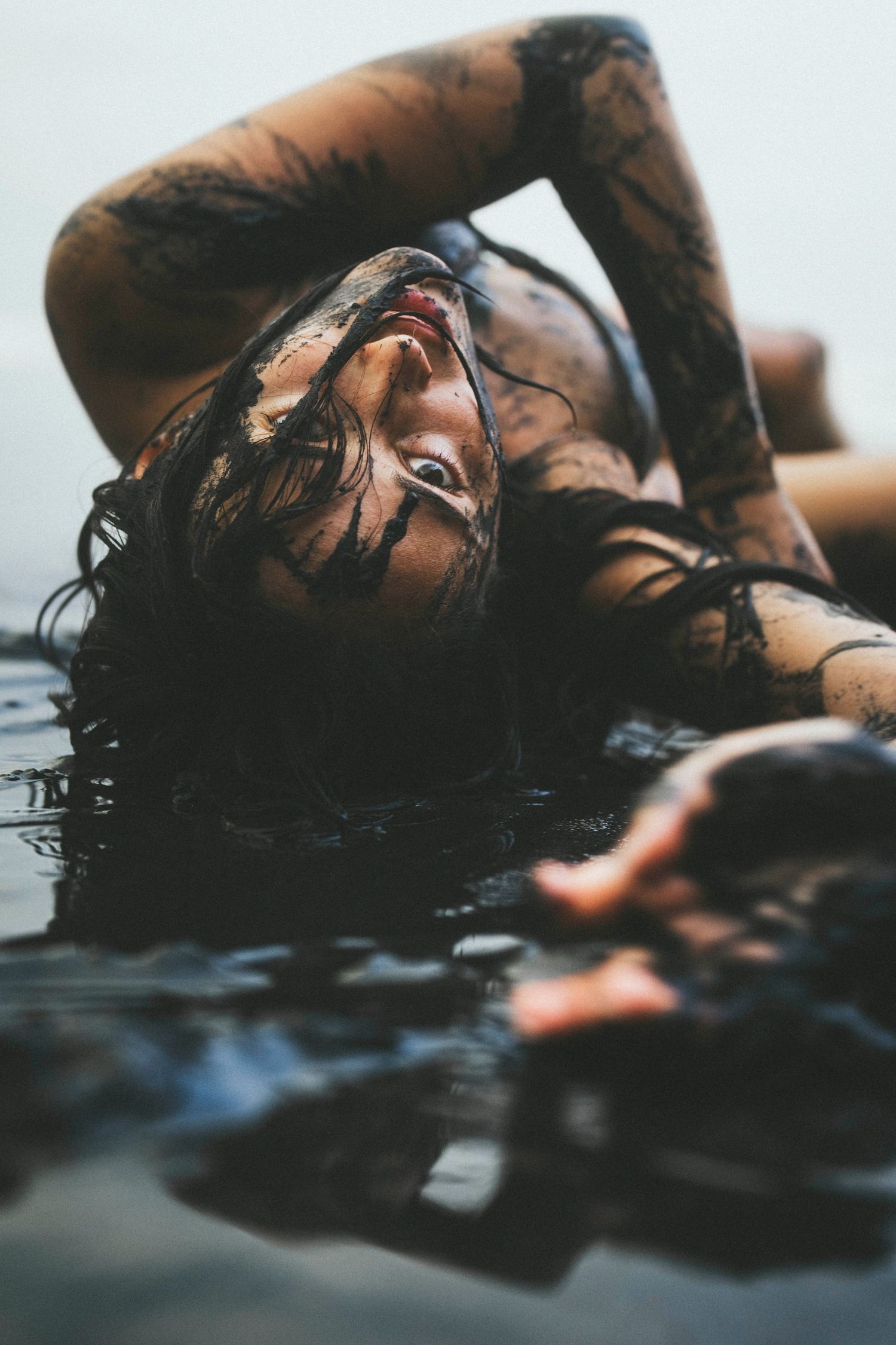 Woman covered in dark mud lying in water, artistic beauty photography concept.