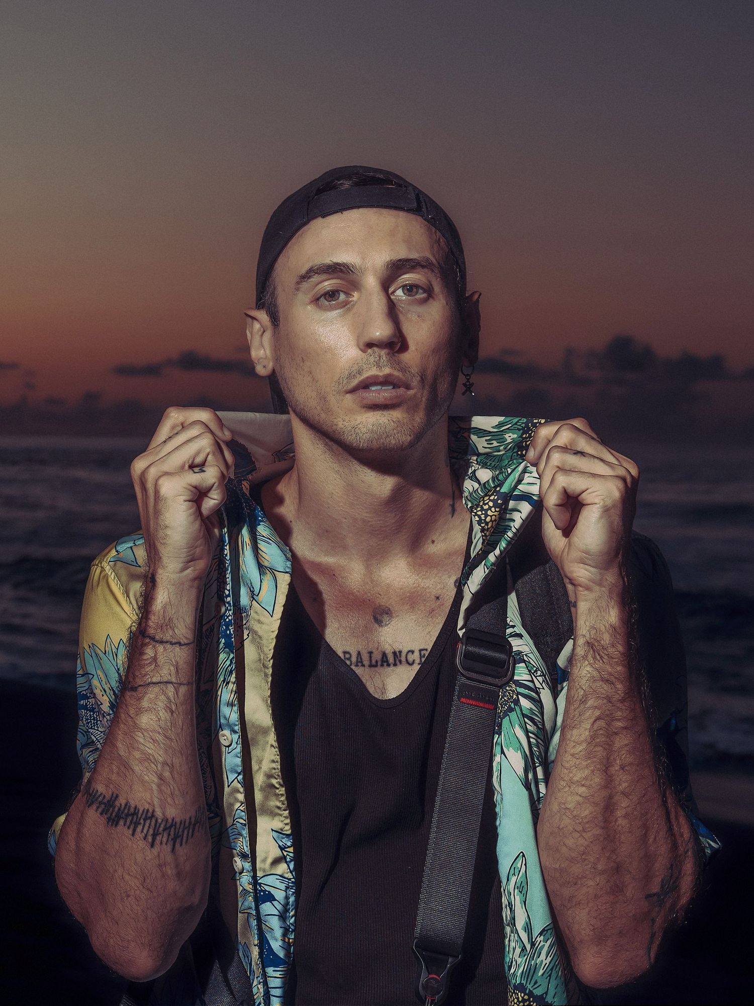Artistic portrait of person wearing black tank top and tropical patterned jacket against vibrant sunset sky.