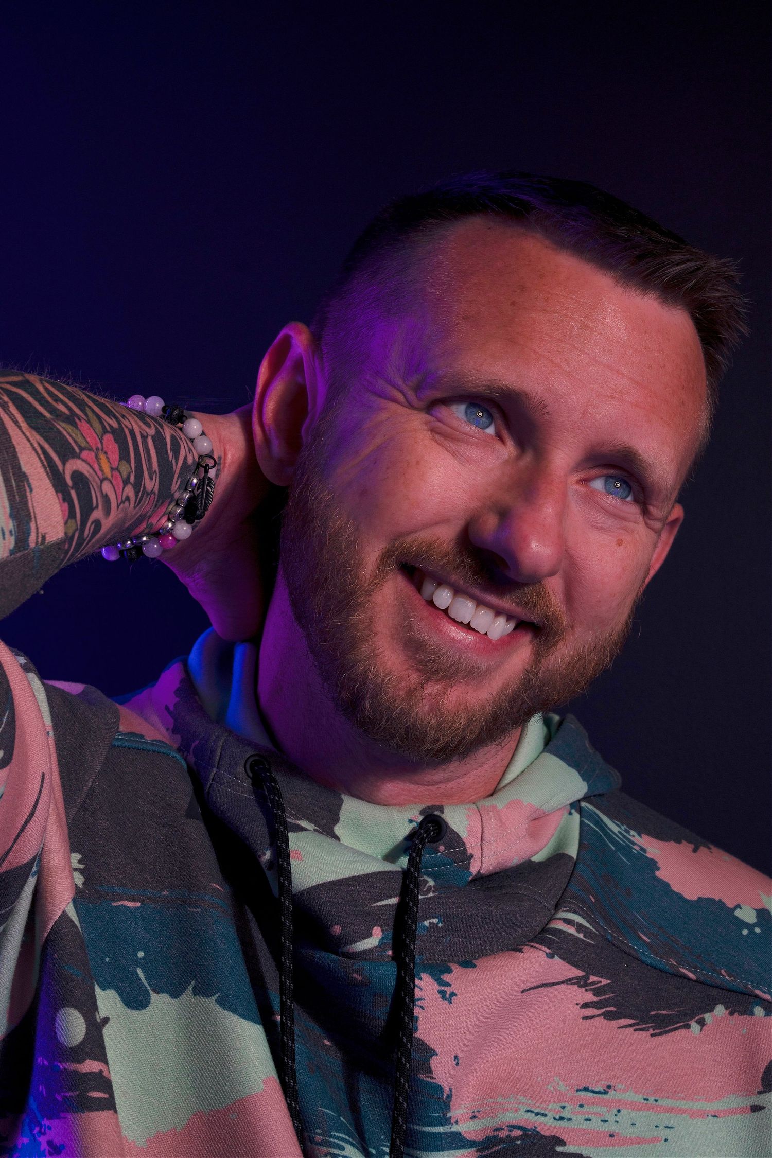 Close-up portrait with purple lighting and camouflage patterned shirt.