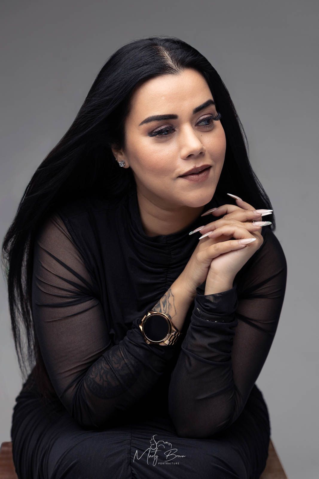 Professional women long sleeved black dress with black hair sitting in front of grey studio backdrop for thoughtfull styled portrait
