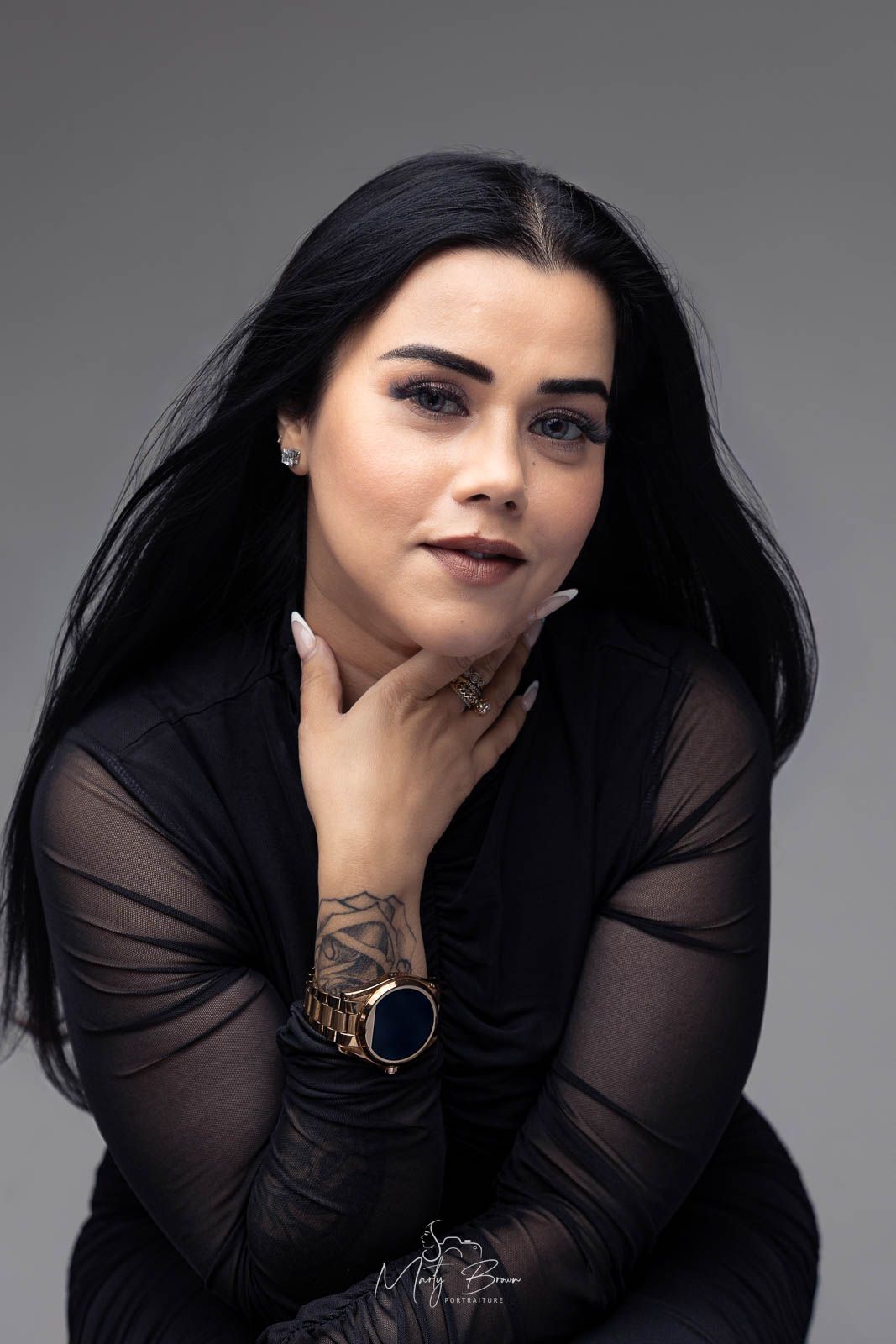 Professional women long sleeved black dress with black hair sitting in front of grey studio backdrop for thoughtfull styled portrait