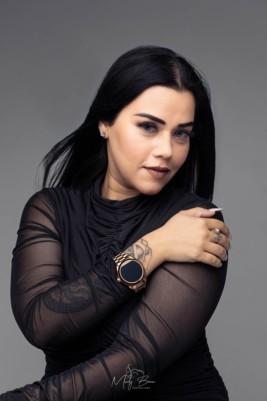 Professional women long sleeved black dress with black hair sitting in front of grey studio backdrop for thoughtfull styled portrait