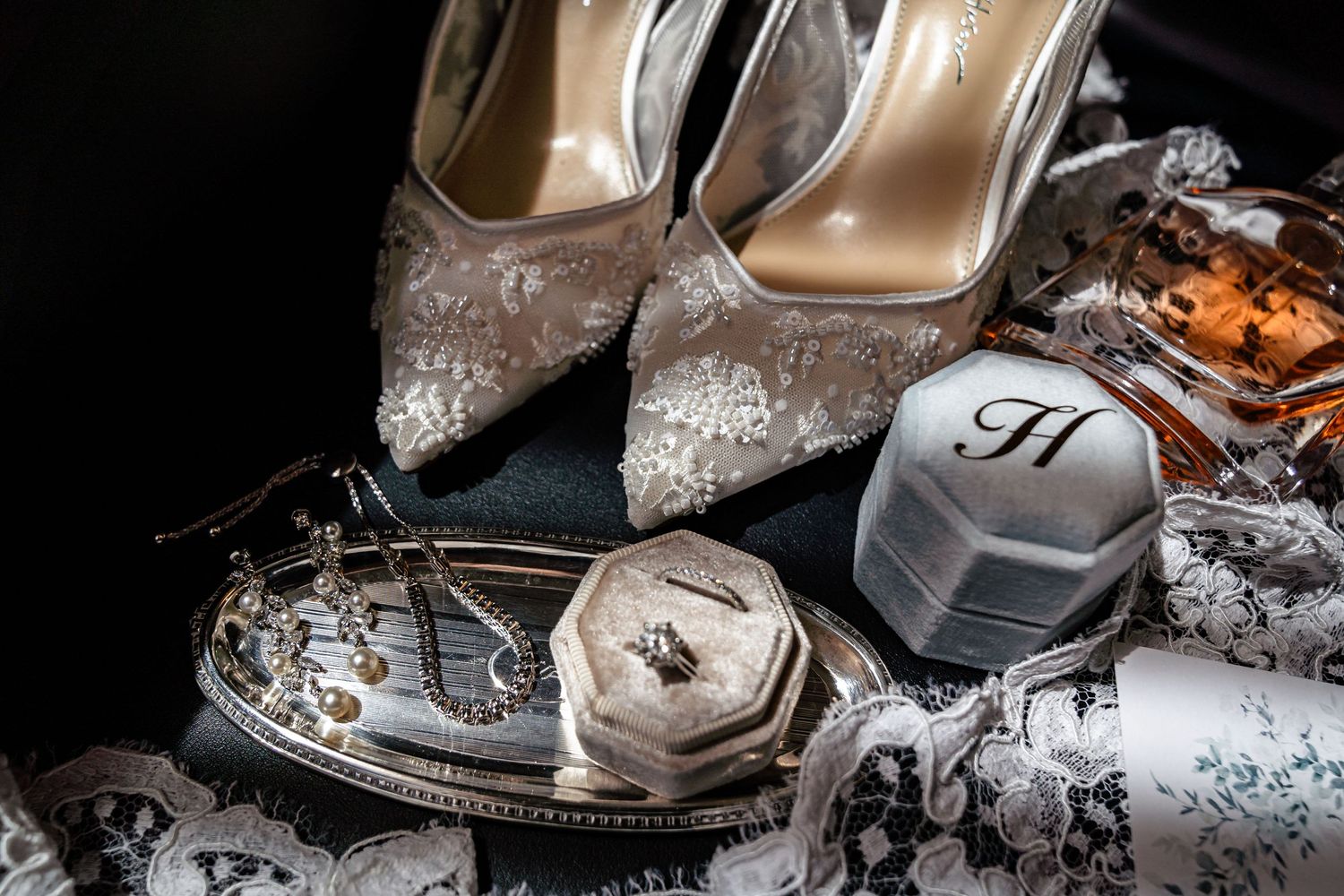 Elegant bridal accessories including sparkly heels, perfume bottle, and lace details arranged on light fabric.