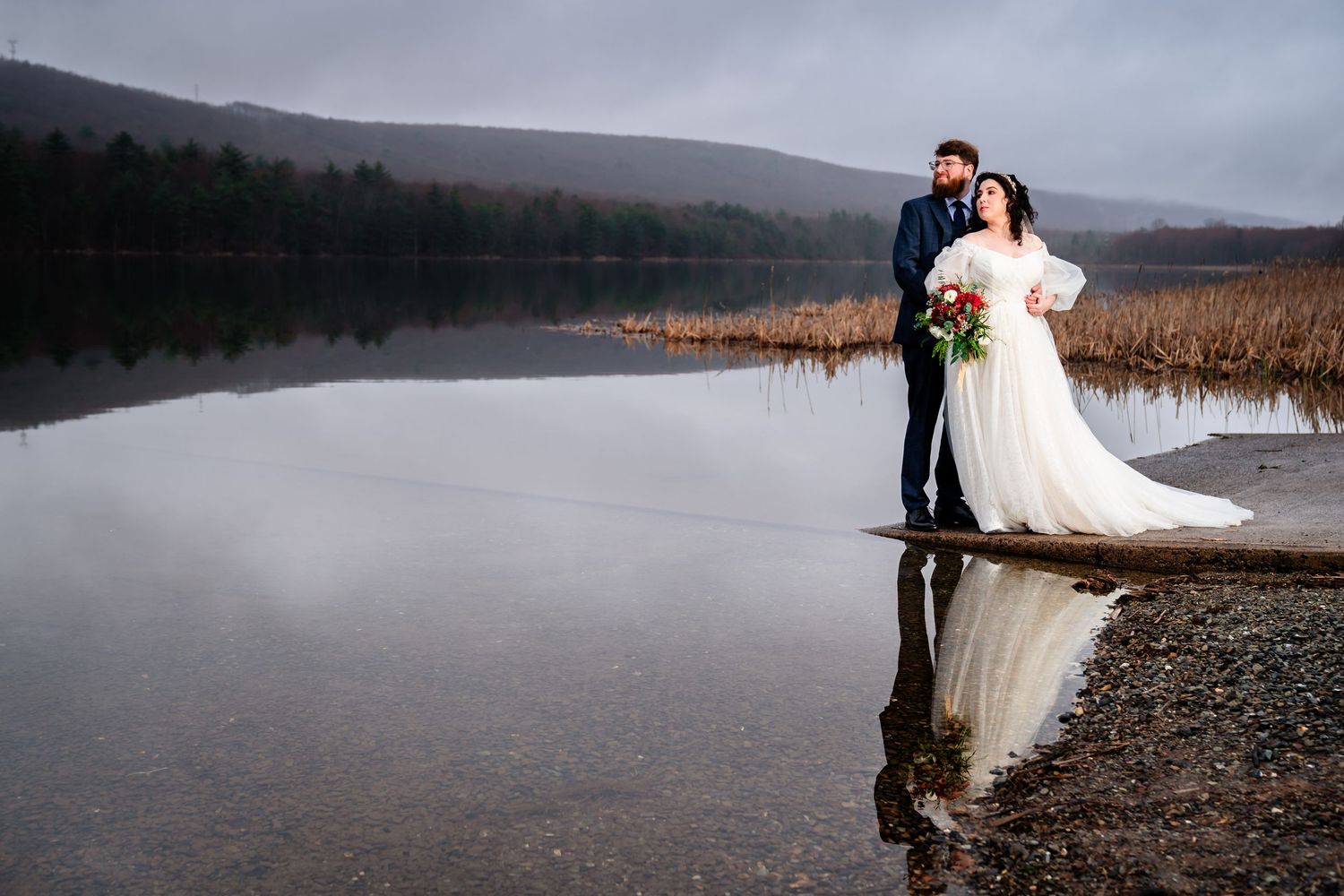Misty lakeside wedding portraits with mountains and cloudy skies in background.
